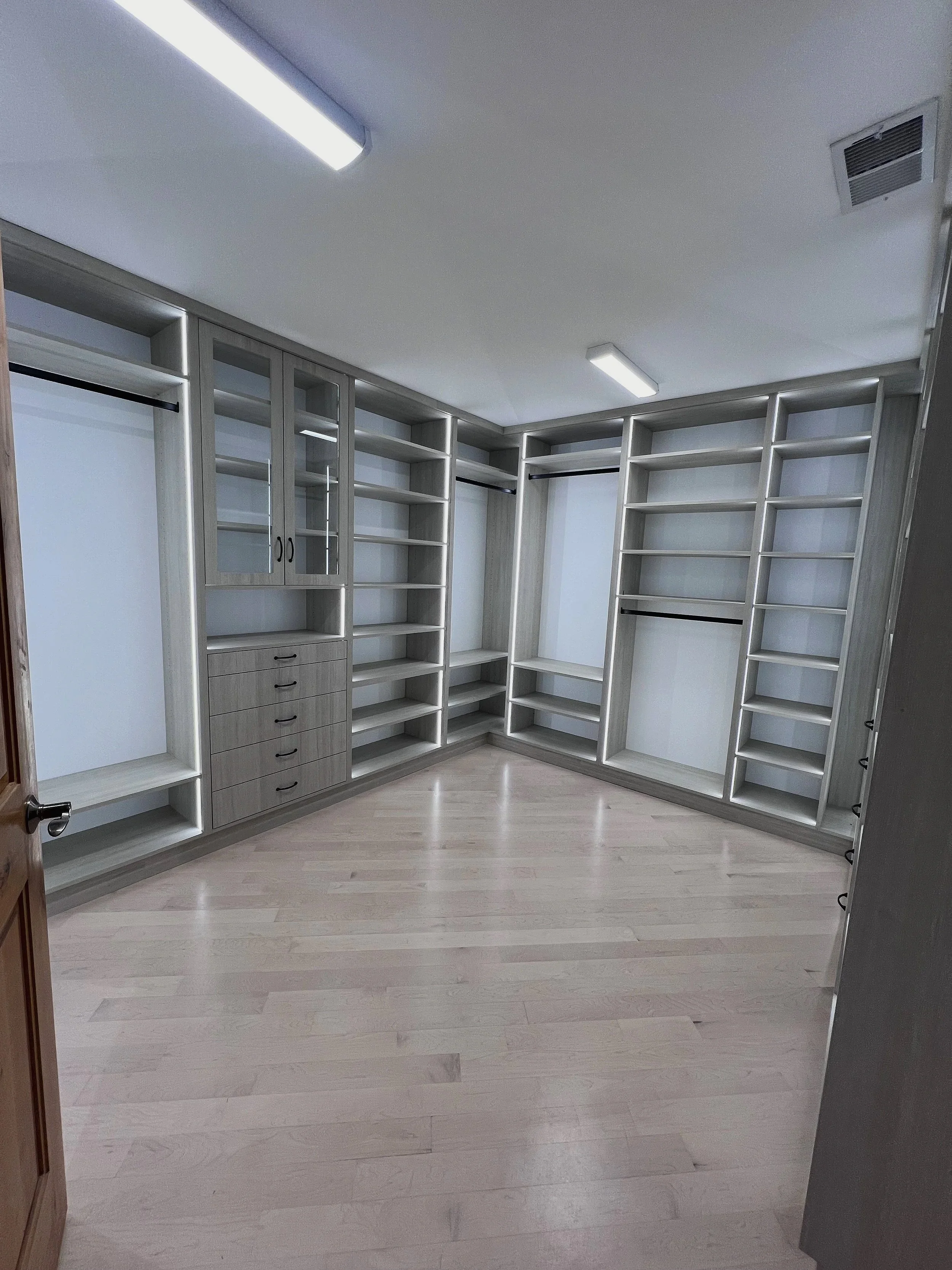 Light gray L-shaped custom walk-in closet system with open shelving and hanging space
