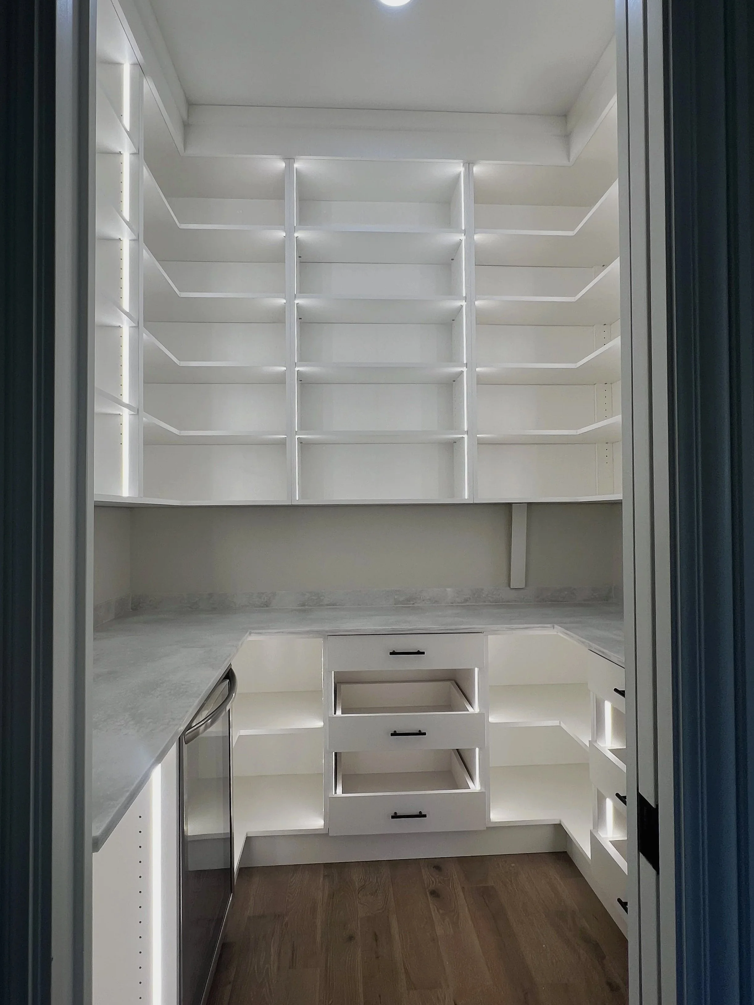 White custom pantry with L-shaped shelving, drawers, and dishwasher below counter