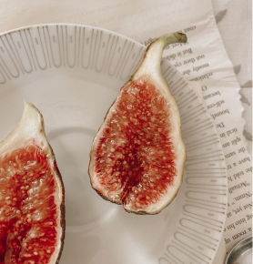 Half of a fresh fig with a pink interior on a white plate.