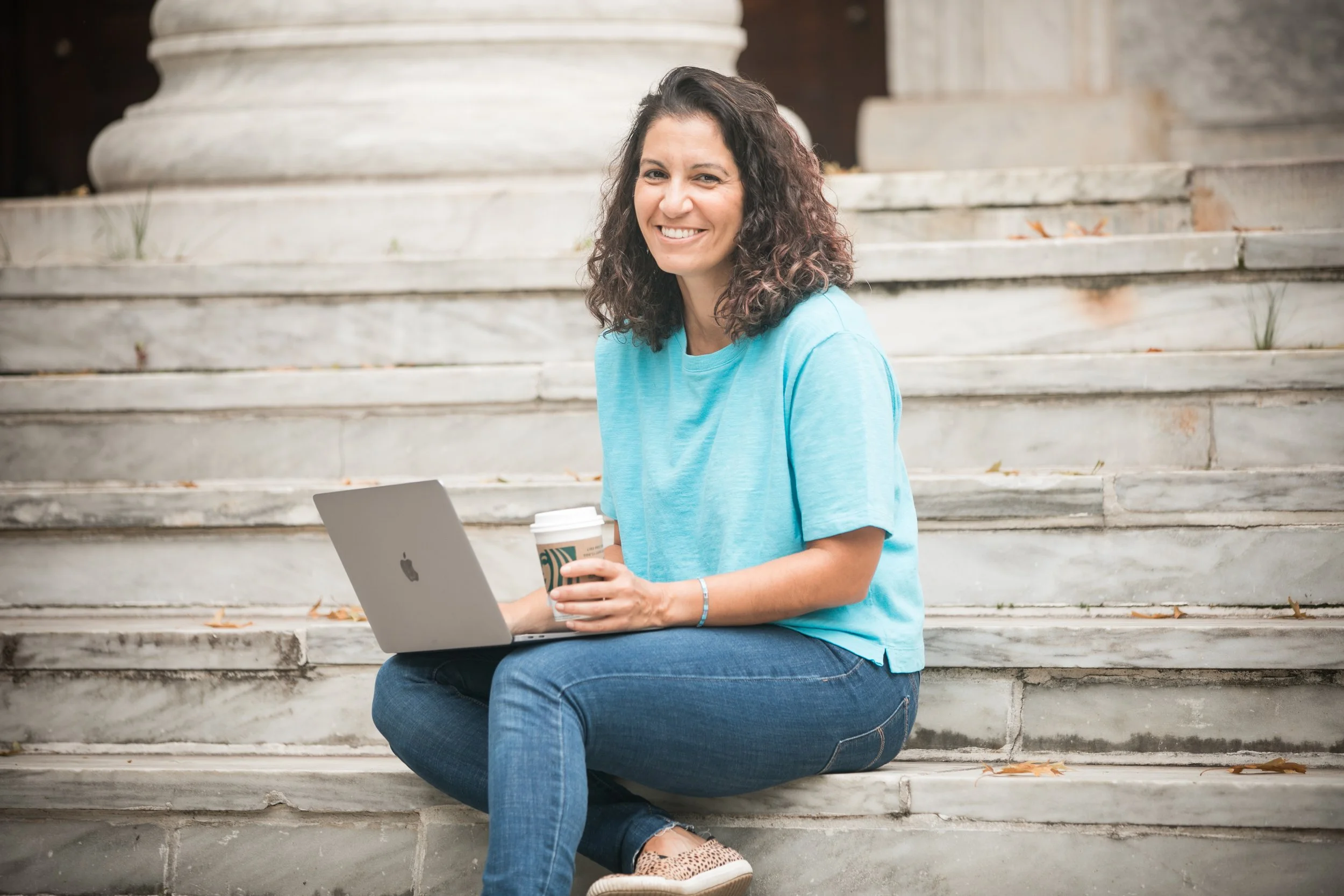 Christine Beck, Professional Resume Writer sitting on marble steps in Princeton, NJ with a laptop and holding a Starbucks coffee cup, smiling