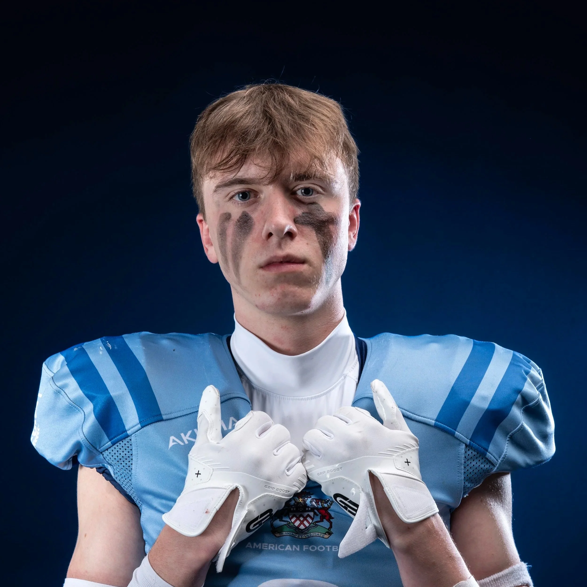 A football player in a light blue jersey and a blue helmet holding a football, standing in front of a blue background with the word 'Glads' and a Spartan logo.