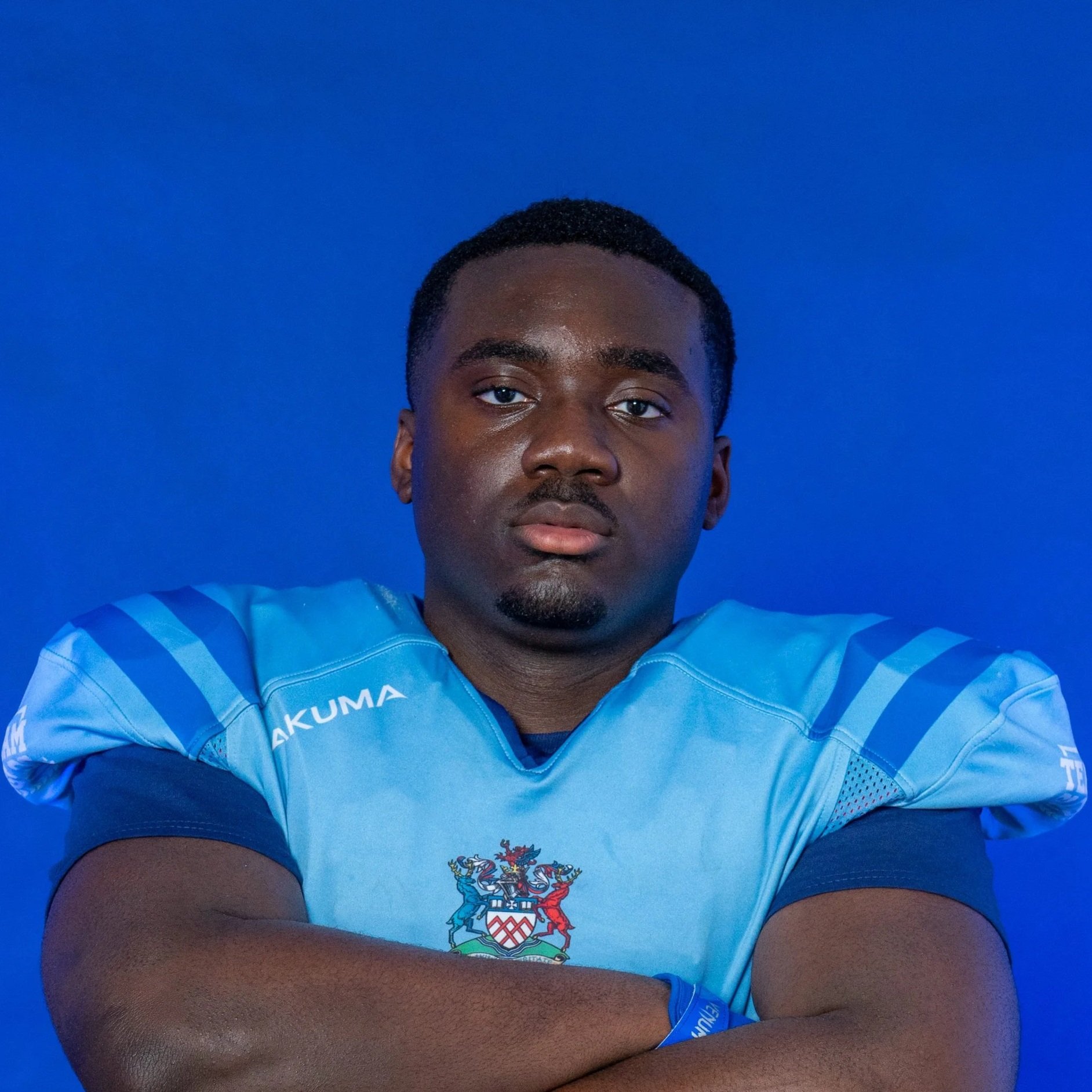Young football player in a blue helmet and jersey holding a football, standing in front of a blue background with 'Glads' and a Spartan helmet logo.