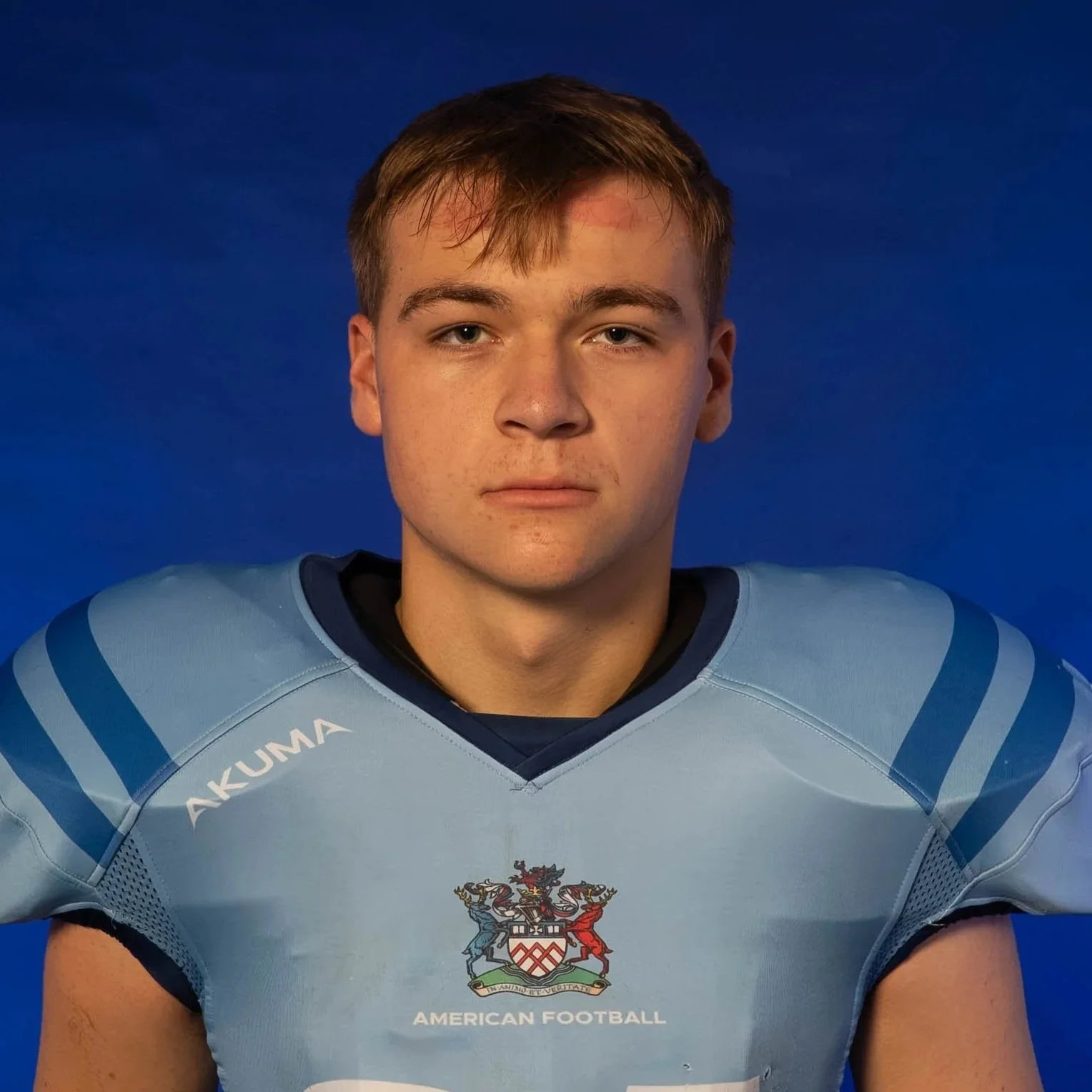 A football player in a blue helmet and jersey, holding a football, standing in front of a Glads team logo background.