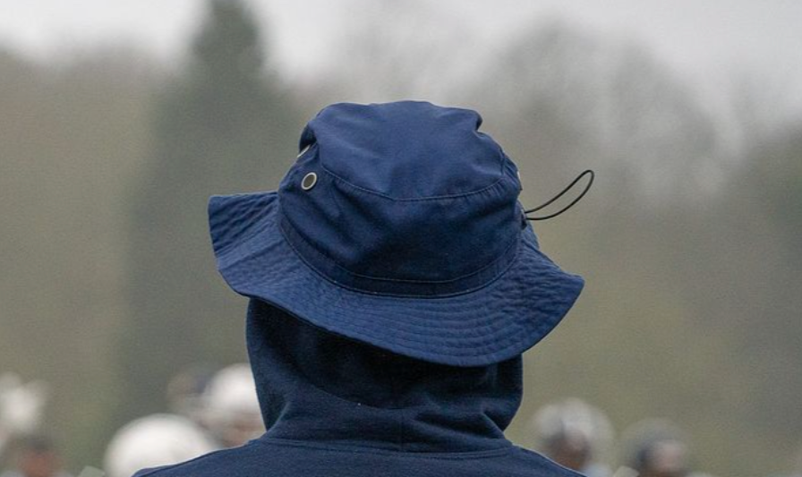 Back of a person wearing a dark hoodie and a blue bucket hat outdoors on a foggy day.