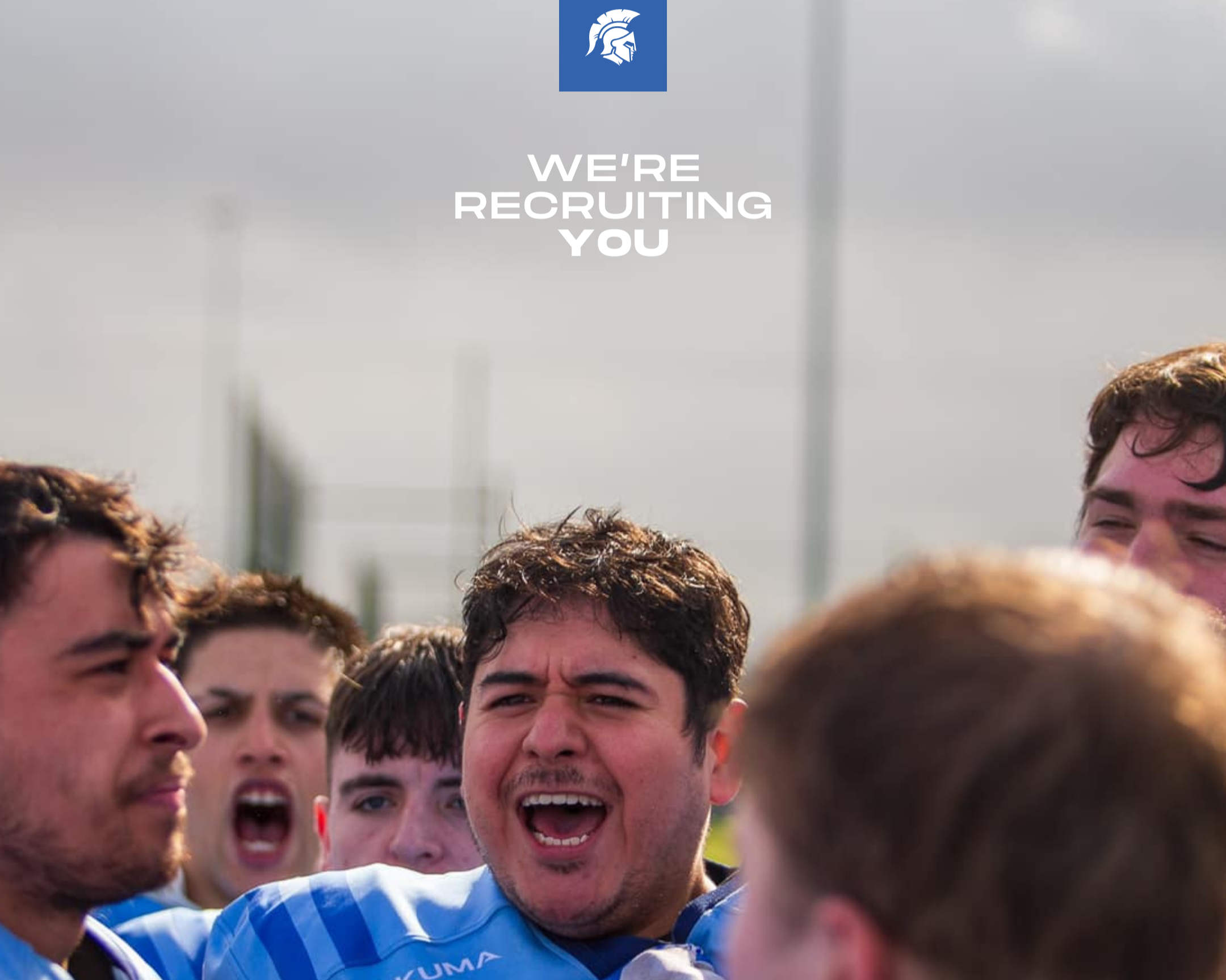 Group of young men gathered together outdoors, some with their mouths open, smiling and expressing excitement. They appear to be celebrating or cheering, with a mostly cloudy sky in the background.