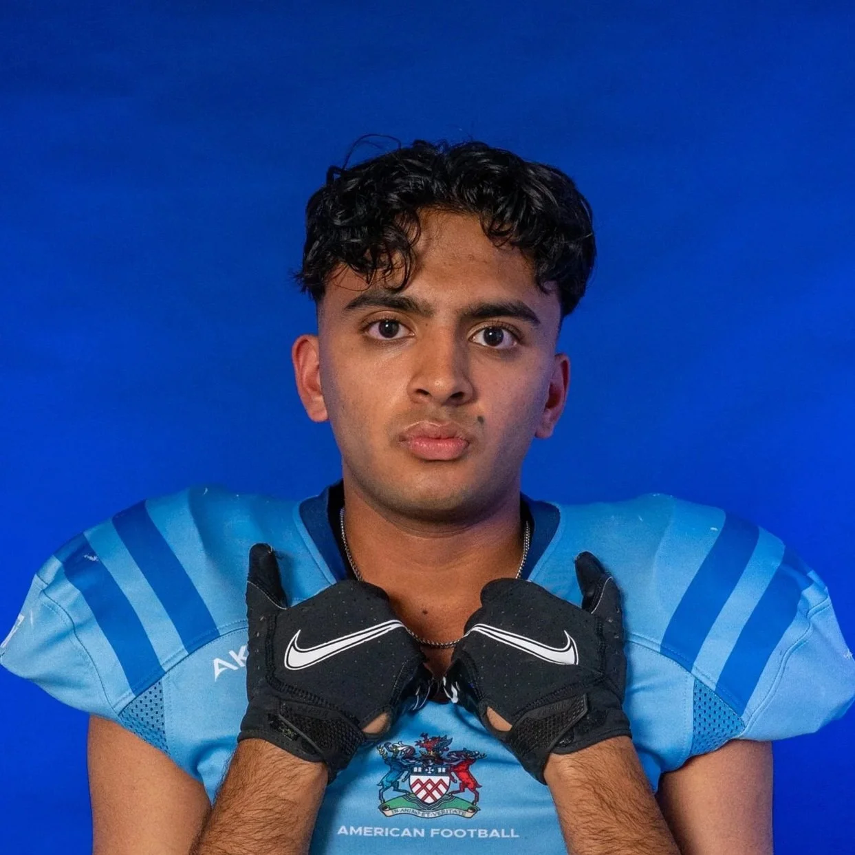 Young football player in a blue helmet and jersey holding a football, standing in front of a GLOVES banner.