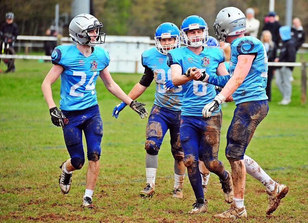 Group of football players in blue uniforms celebrating on a muddy field