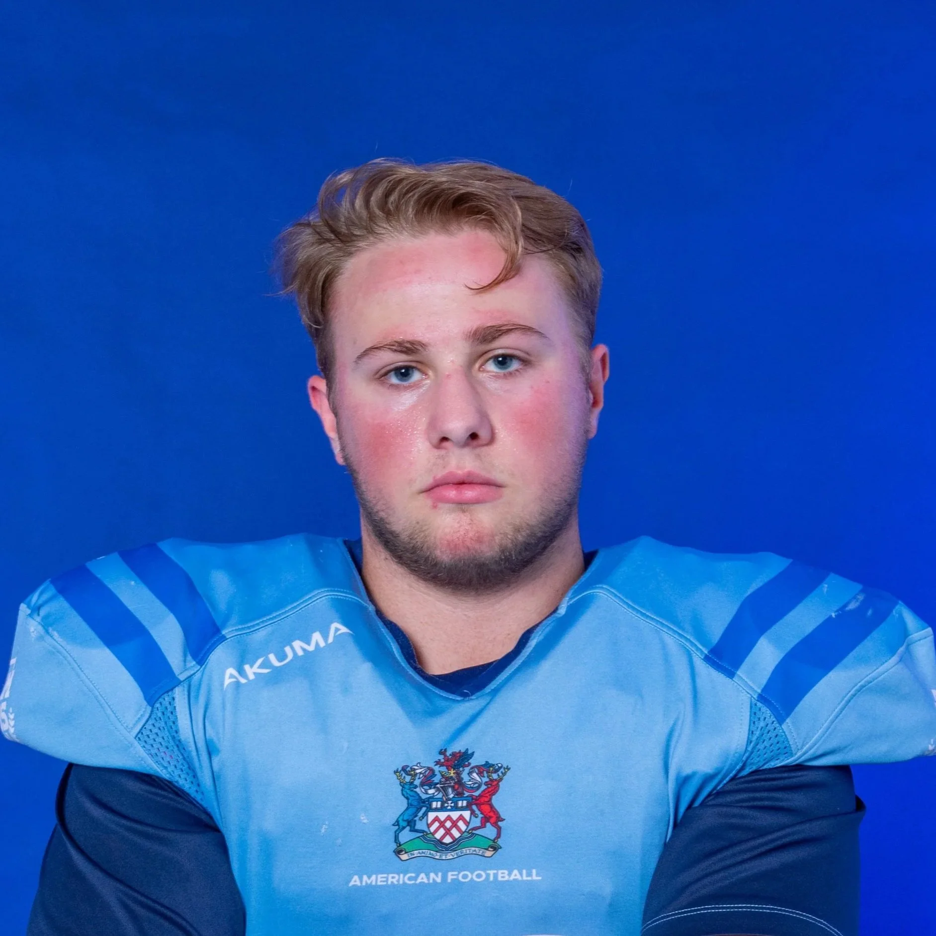A football player in a blue helmet and jersey holding a football, standing in front of a blue background with the Glads logo.