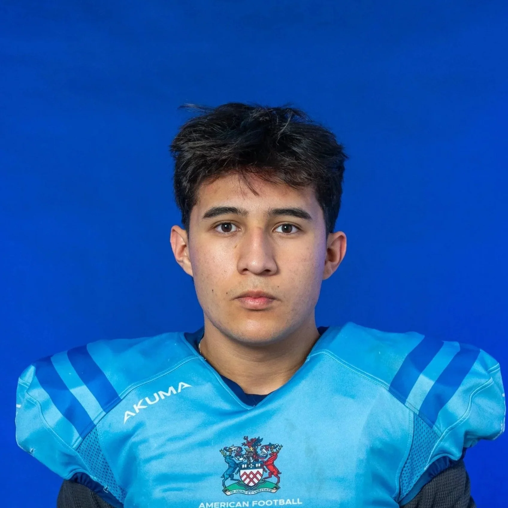 A football player in a blue helmet and light blue jersey holding a football, standing against a dark background with the word 'Glads' in large white letters.