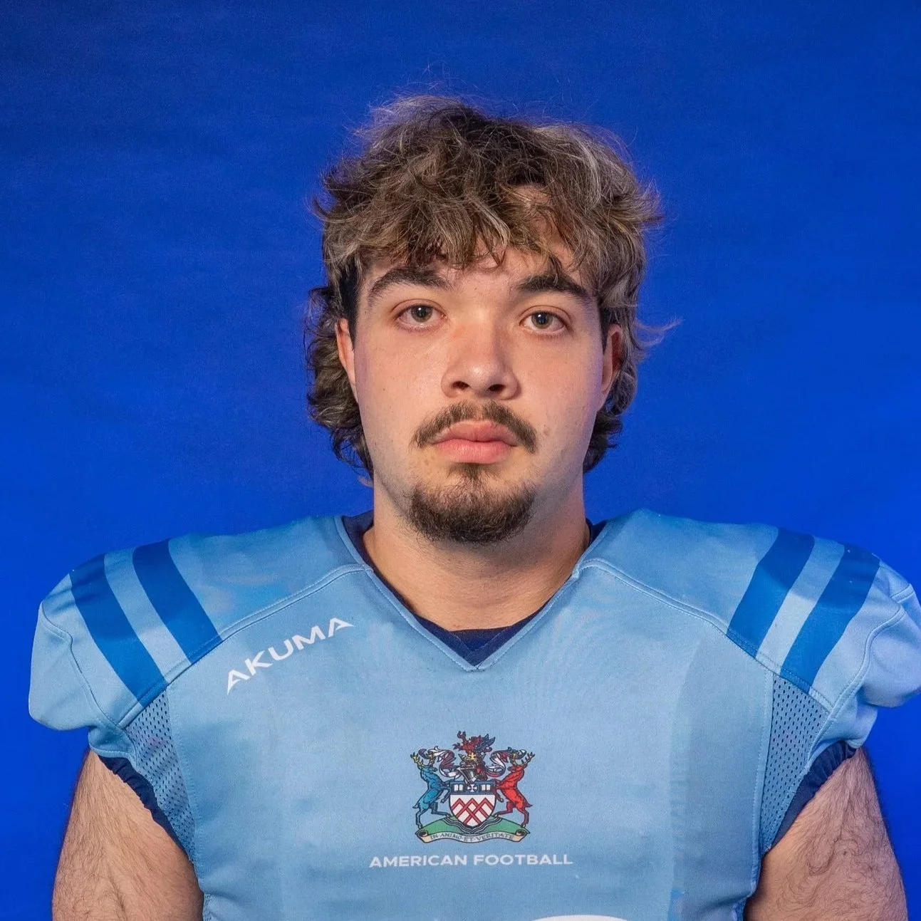 A football player in a blue helmet and jersey holding a football, standing in front of a GLOVIS logo background.
