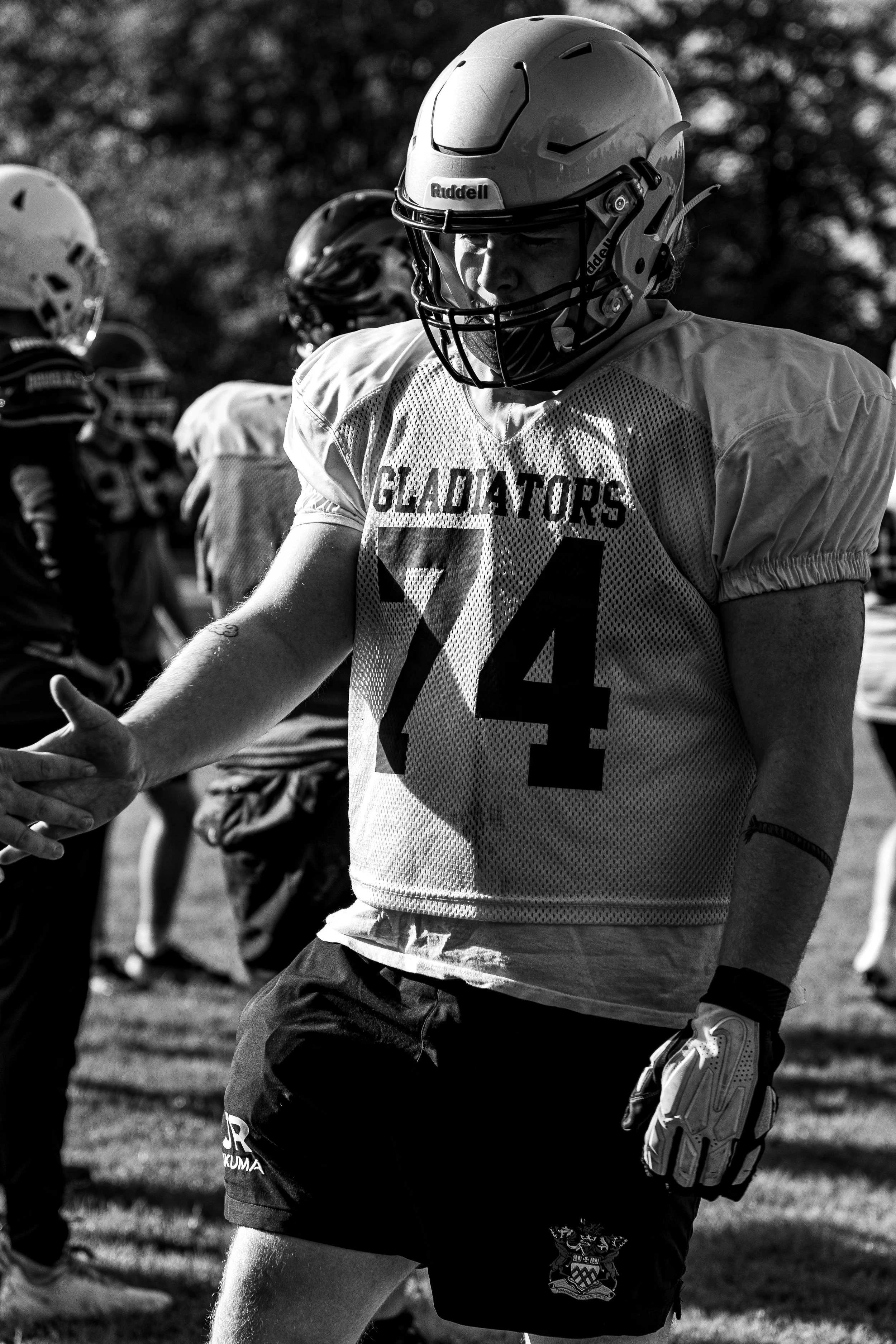 A football player in a helmet and jersey with the number 74, reaching out to shake hands with another player during a game or practice.