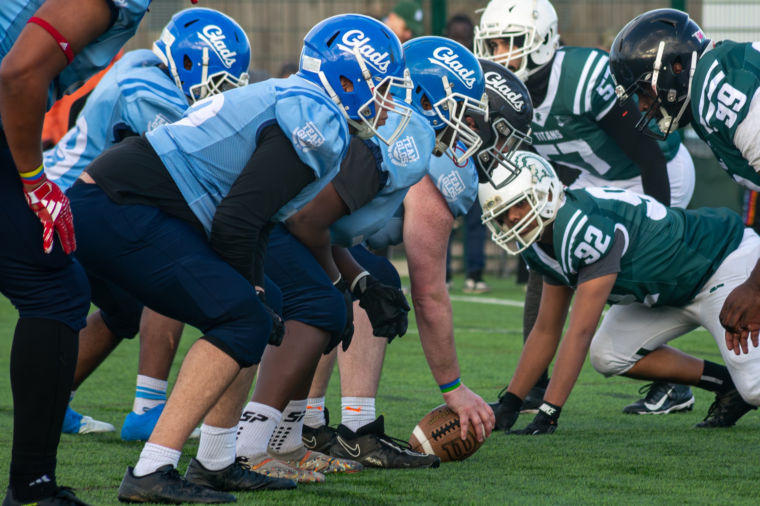 American football players lined up in formation on the field during a game, with the ball on the ground ready for the snap.