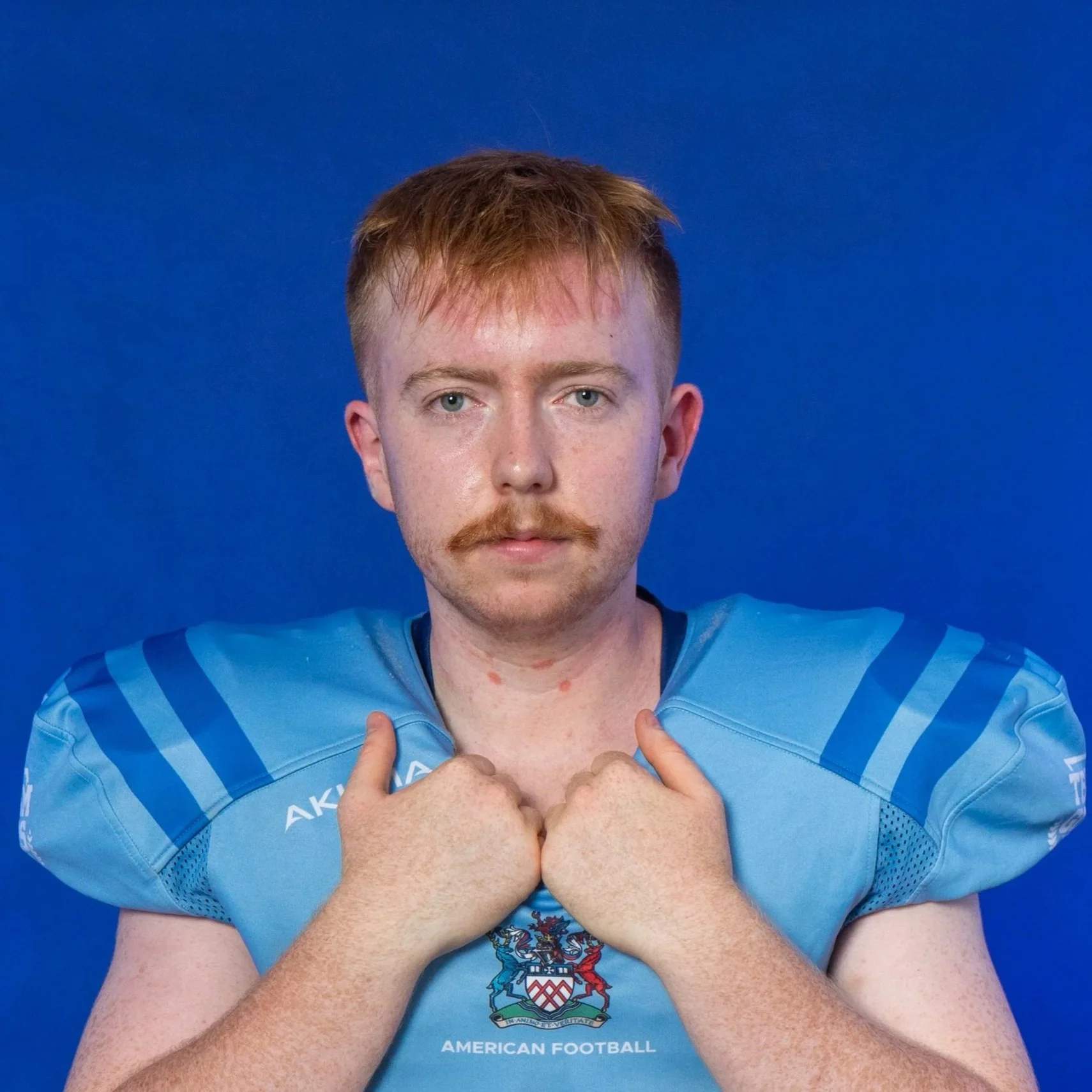 American football player wearing a blue helmet and jersey with Glads logo, holding a football, against a blue background with Glads logo.