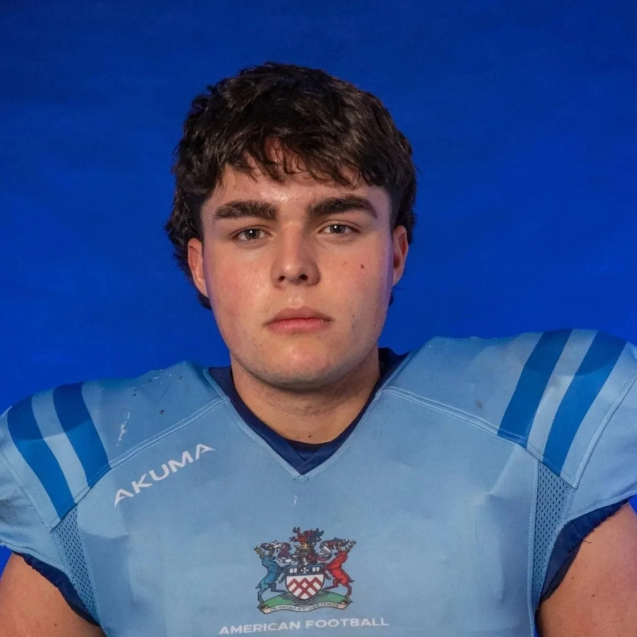 Football player in blue helmet and jersey holding a football against a blue background with the Glogs logo.