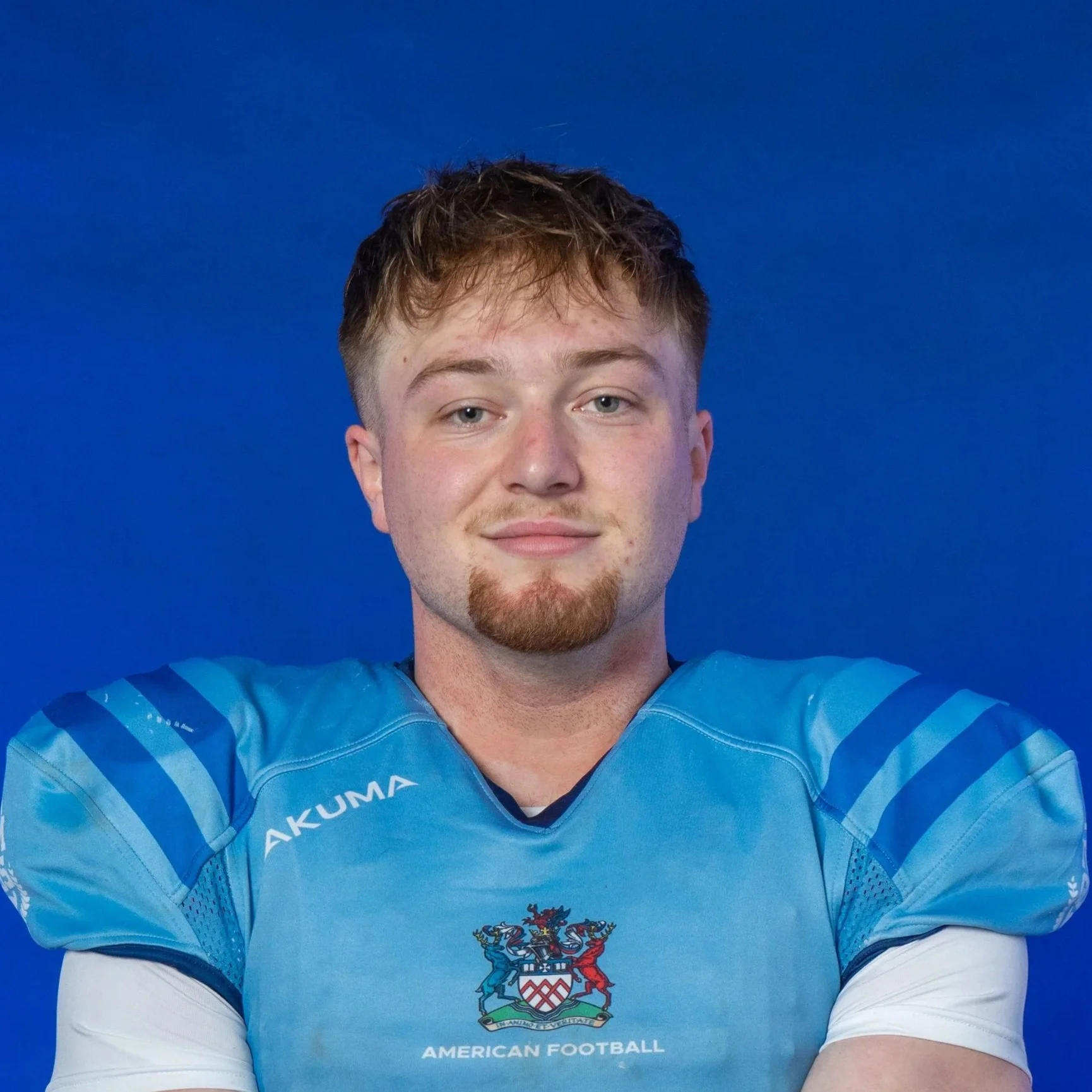 A football player in a light blue helmet and jersey holding a football, standing in front of a blue background with the Glads logo.