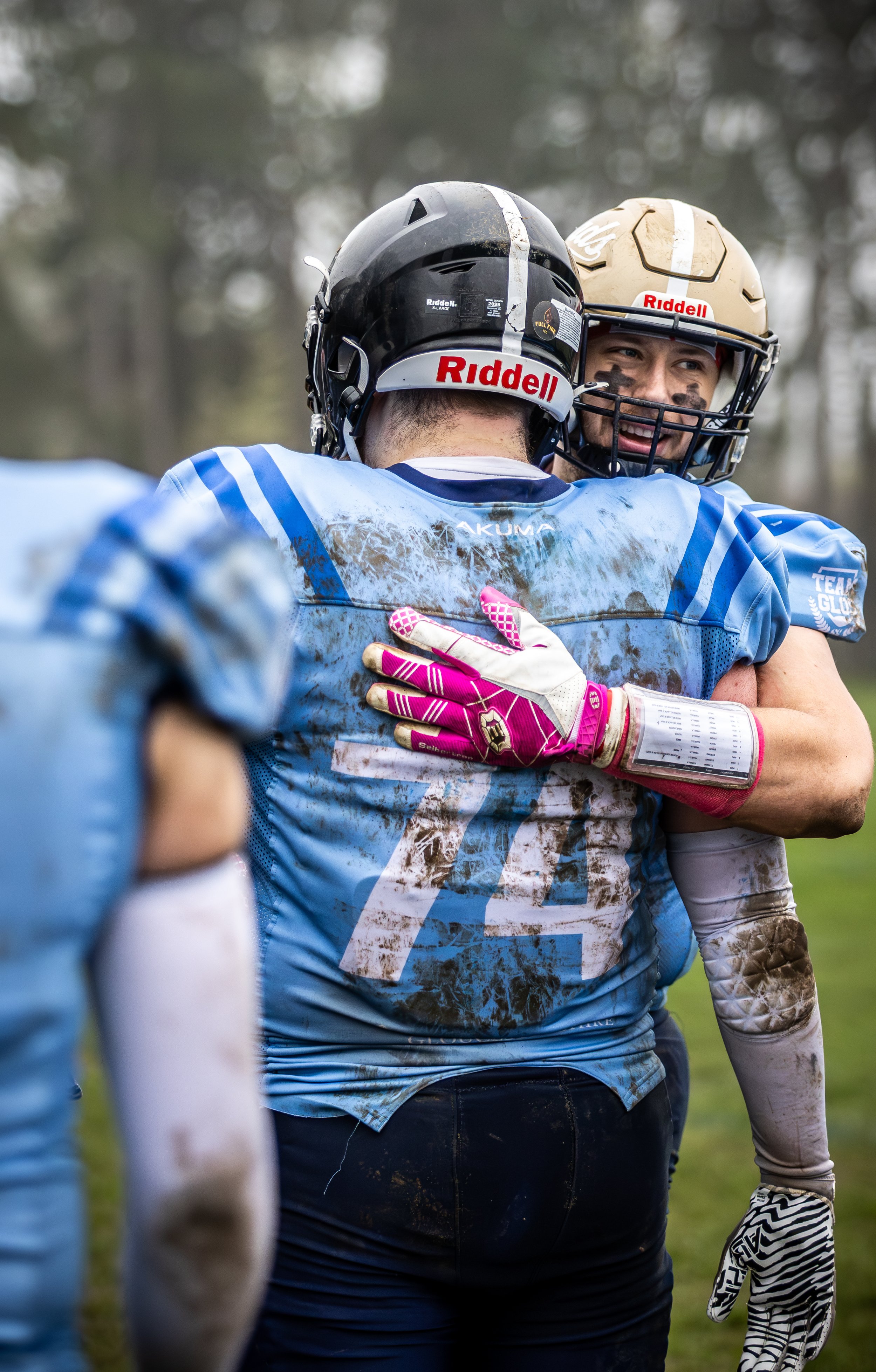 Two football players wearing helmets and uniforms hugging on the field during a game.