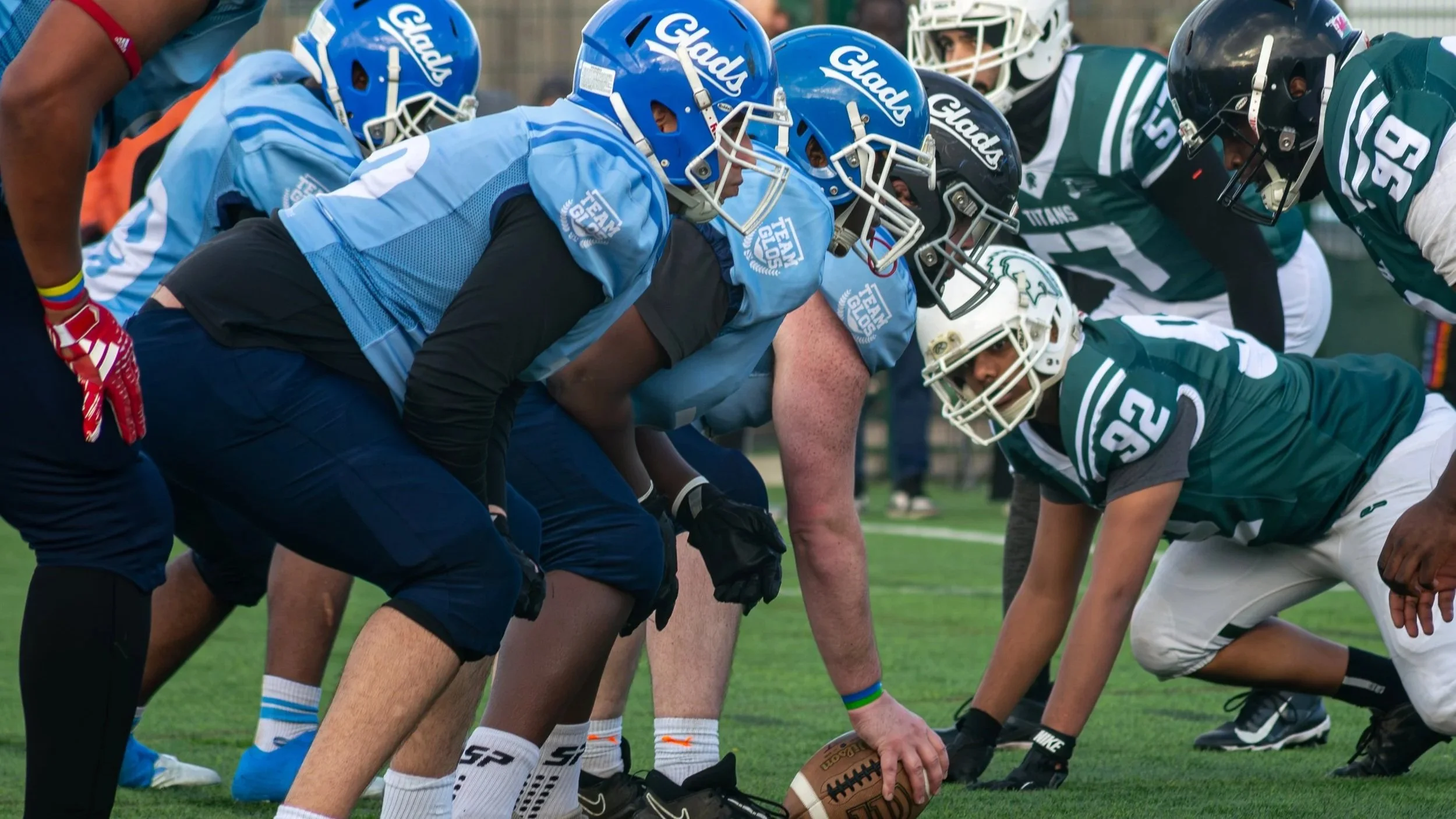 American football players from opposing teams lined up at the line of scrimmage, preparing for the snap of the ball during a game.
