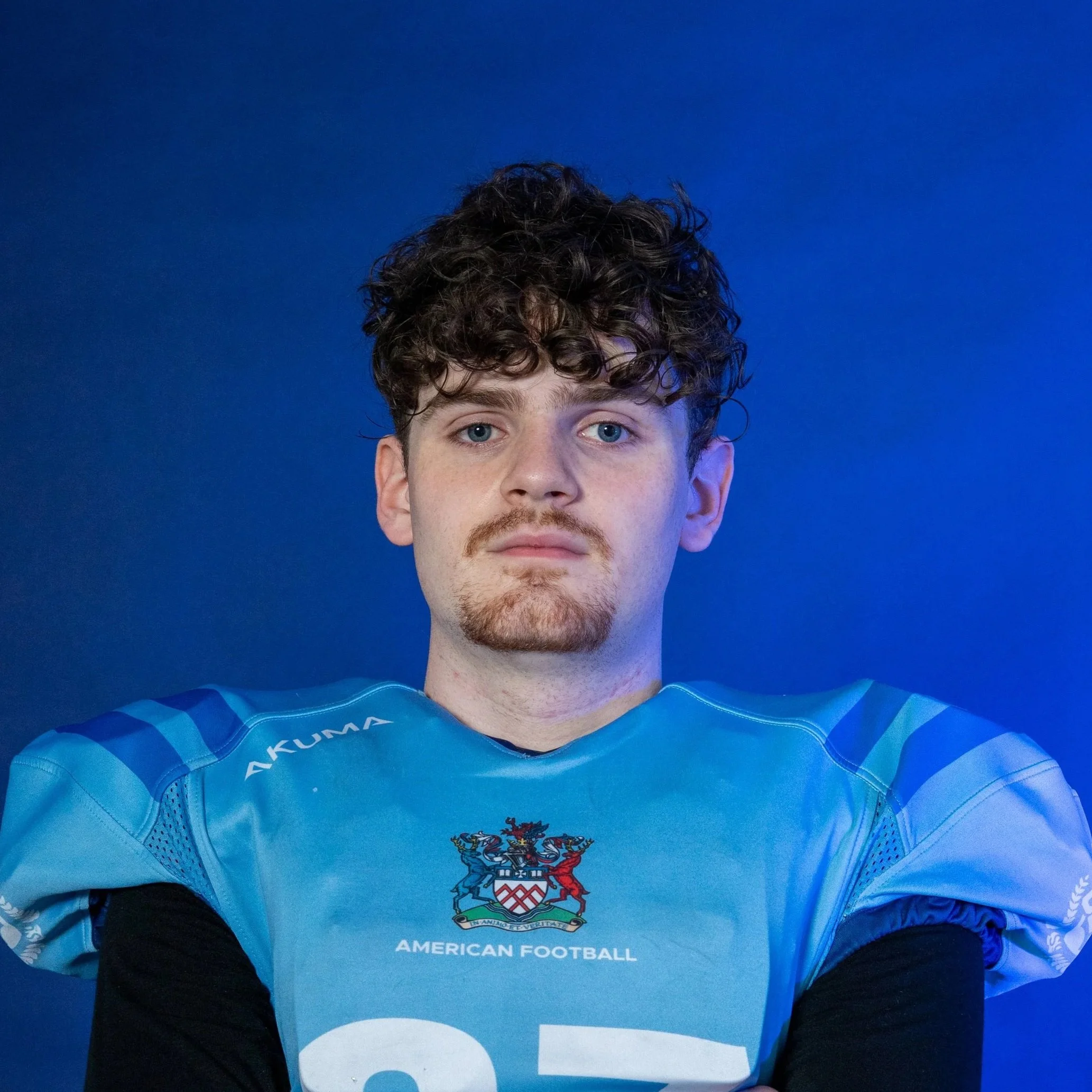 A football player in a blue helmet and jersey holding a football in front of a backdrop with the Gloats logo.