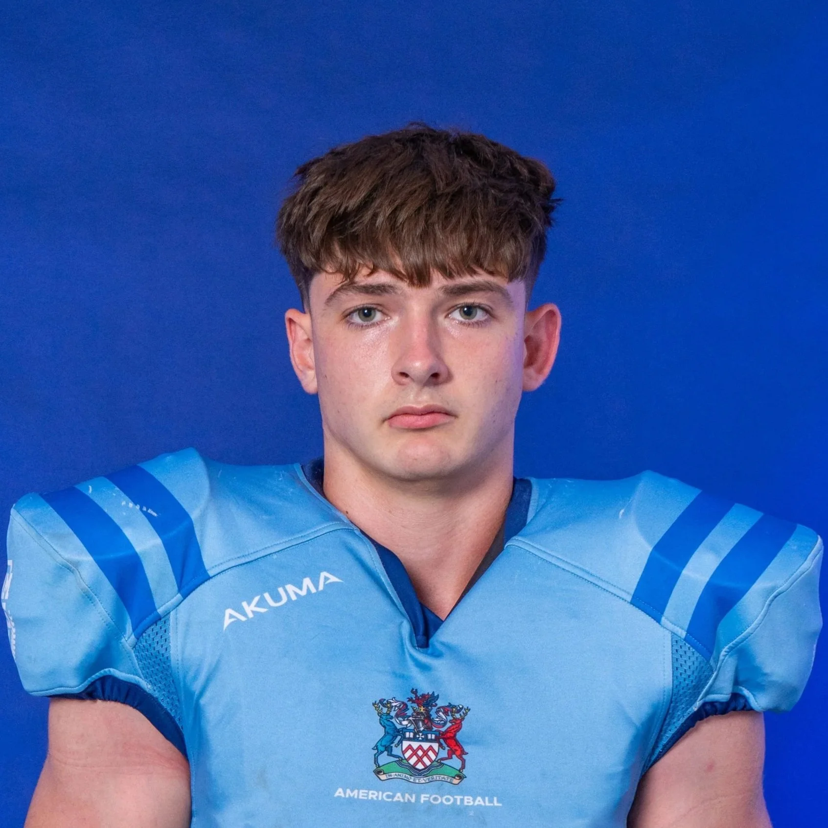 Football player in light blue and black uniform holding a football, wearing a blue helmet with 'Glads' written on it, standing in front of a dark blue background with 'Glads' logo and text.