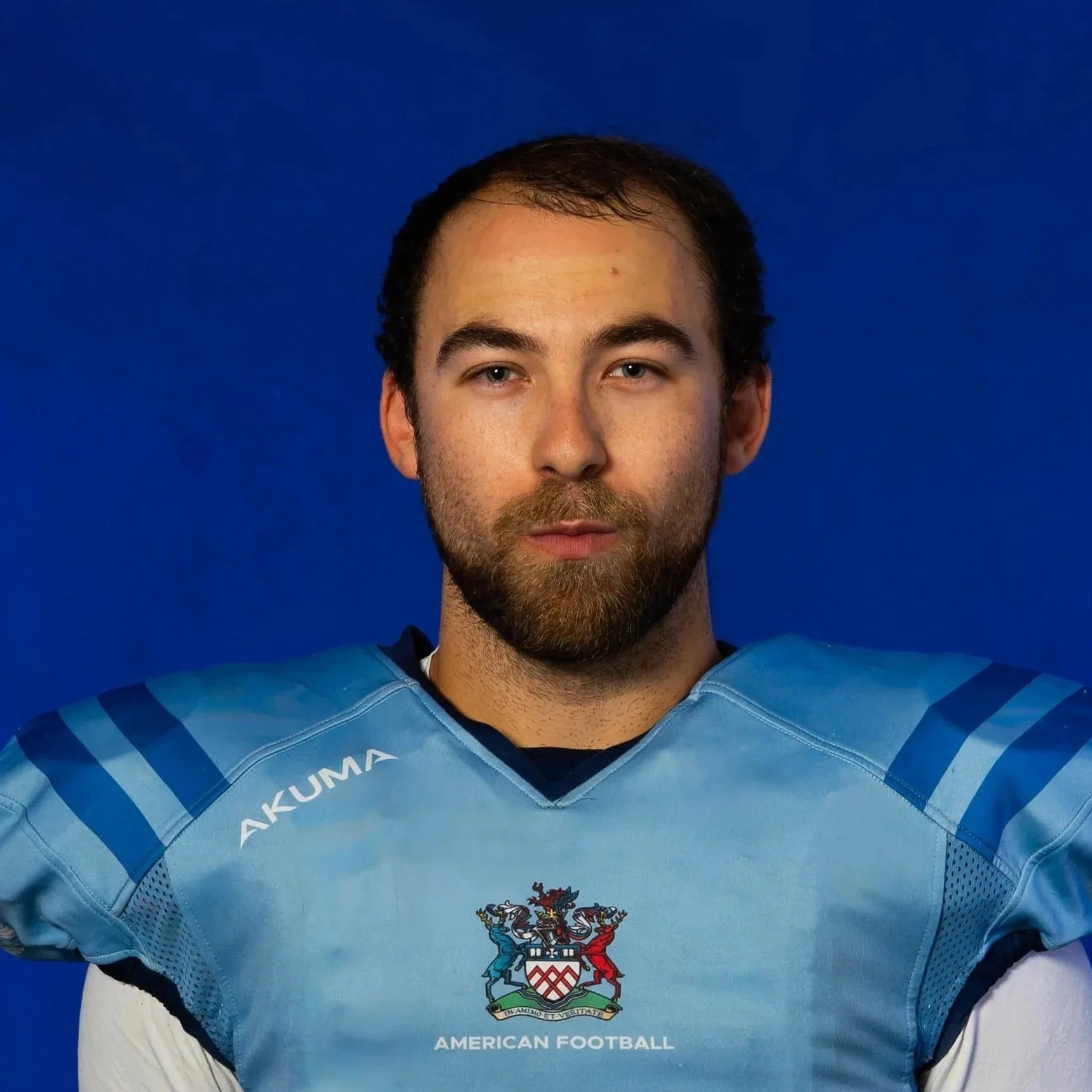 Portrait of a male American football player wearing a blue helmet and jersey, standing against a dark background.
