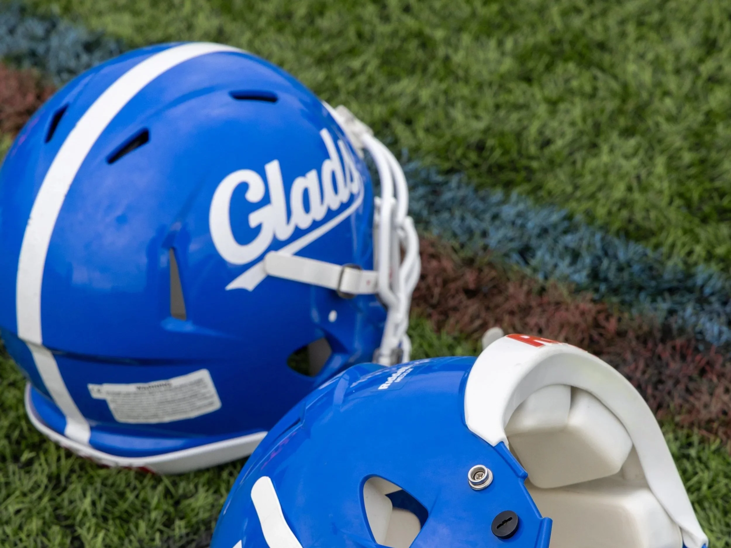 A blue football helmet with white accents lying on a grassy field.