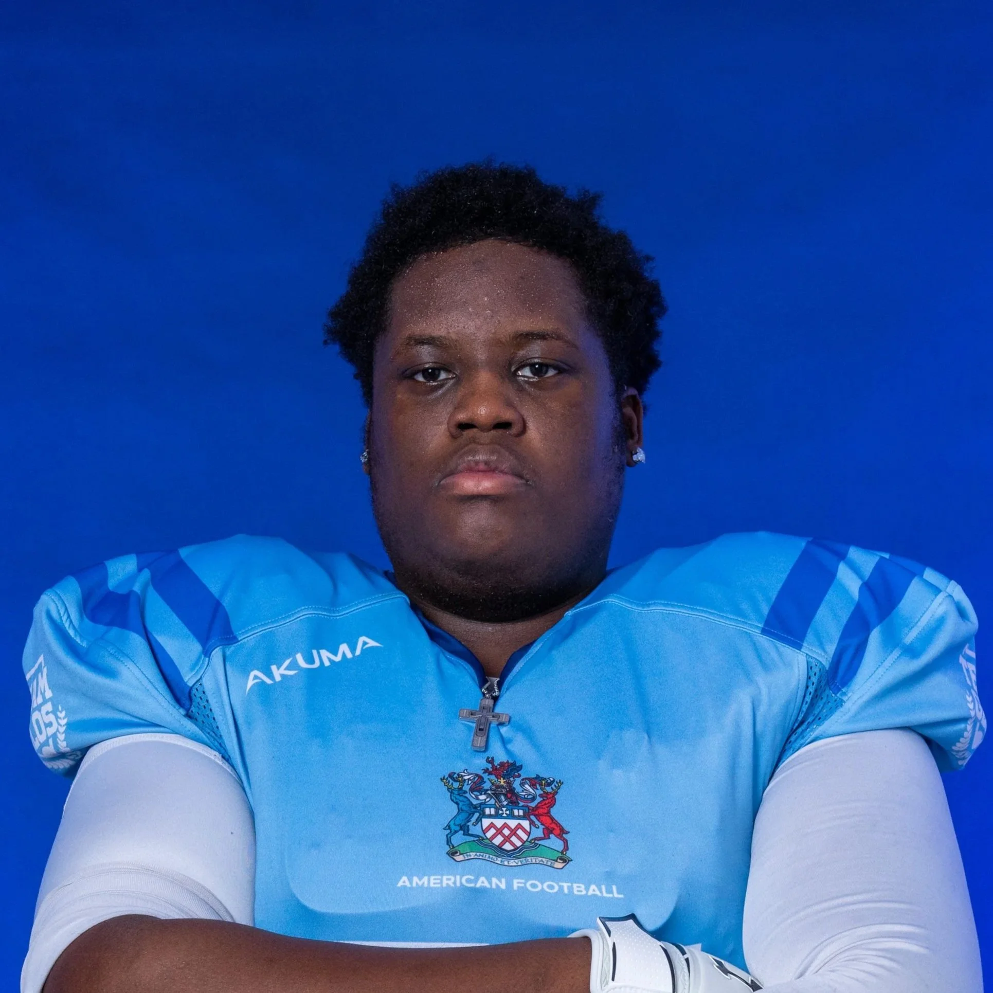 A football player in a blue helmet and jersey, wearing football gloves, standing against a dark background.