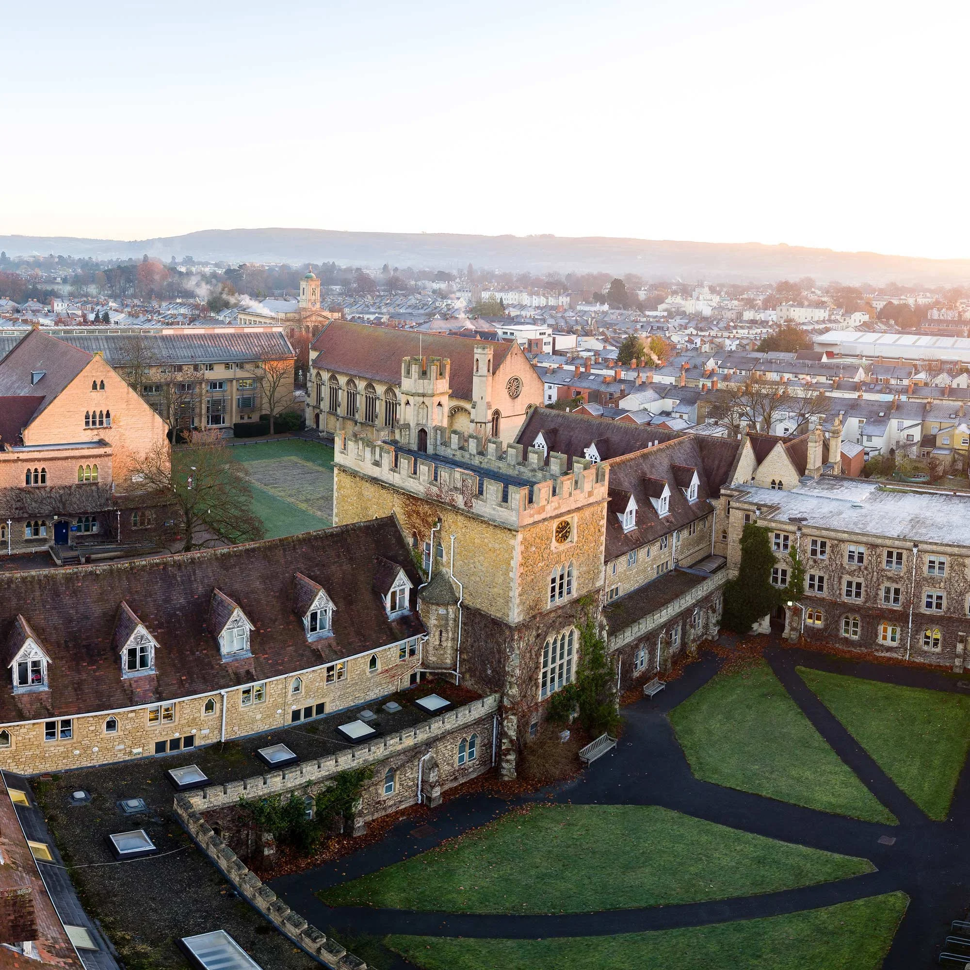 An aerial view of a historic castle with a lush green lawn and a town in the background, during sunset.