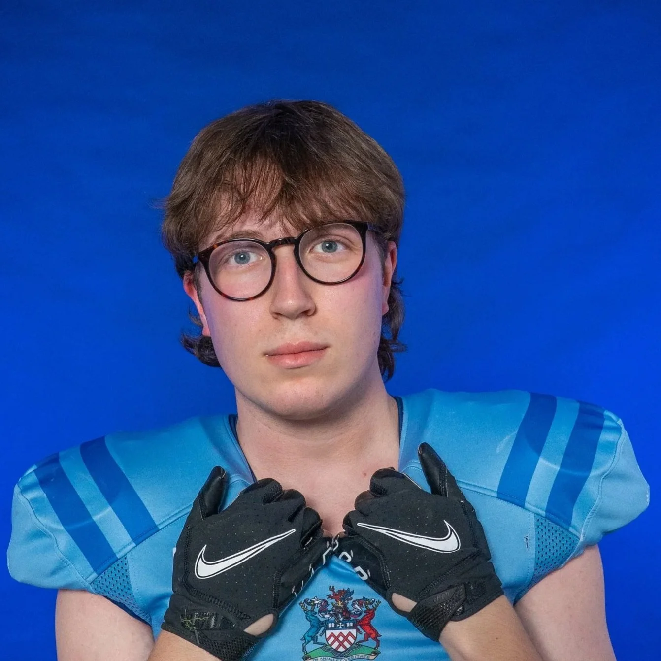A football player wearing a blue helmet and shoulder pads, holding a football, with a blue background featuring the Glad's logo and a Michigan State Spartans logo.