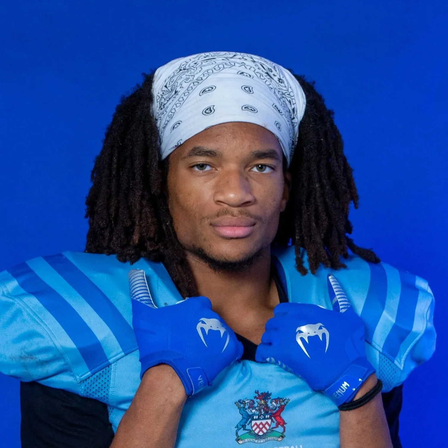 A football player in a blue Glads helmet and jersey, holding a football, standing in front of a Glads logo background.