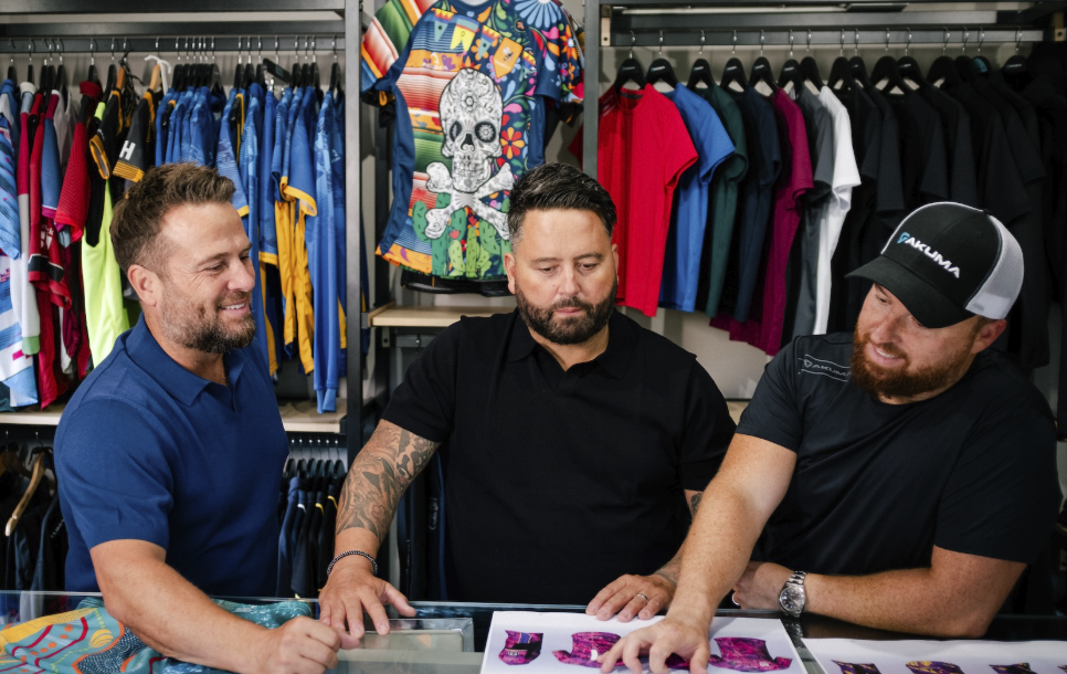 Three men shopping for sports apparel in a store, with colorful clothing and graphic T-shirts displayed behind them.