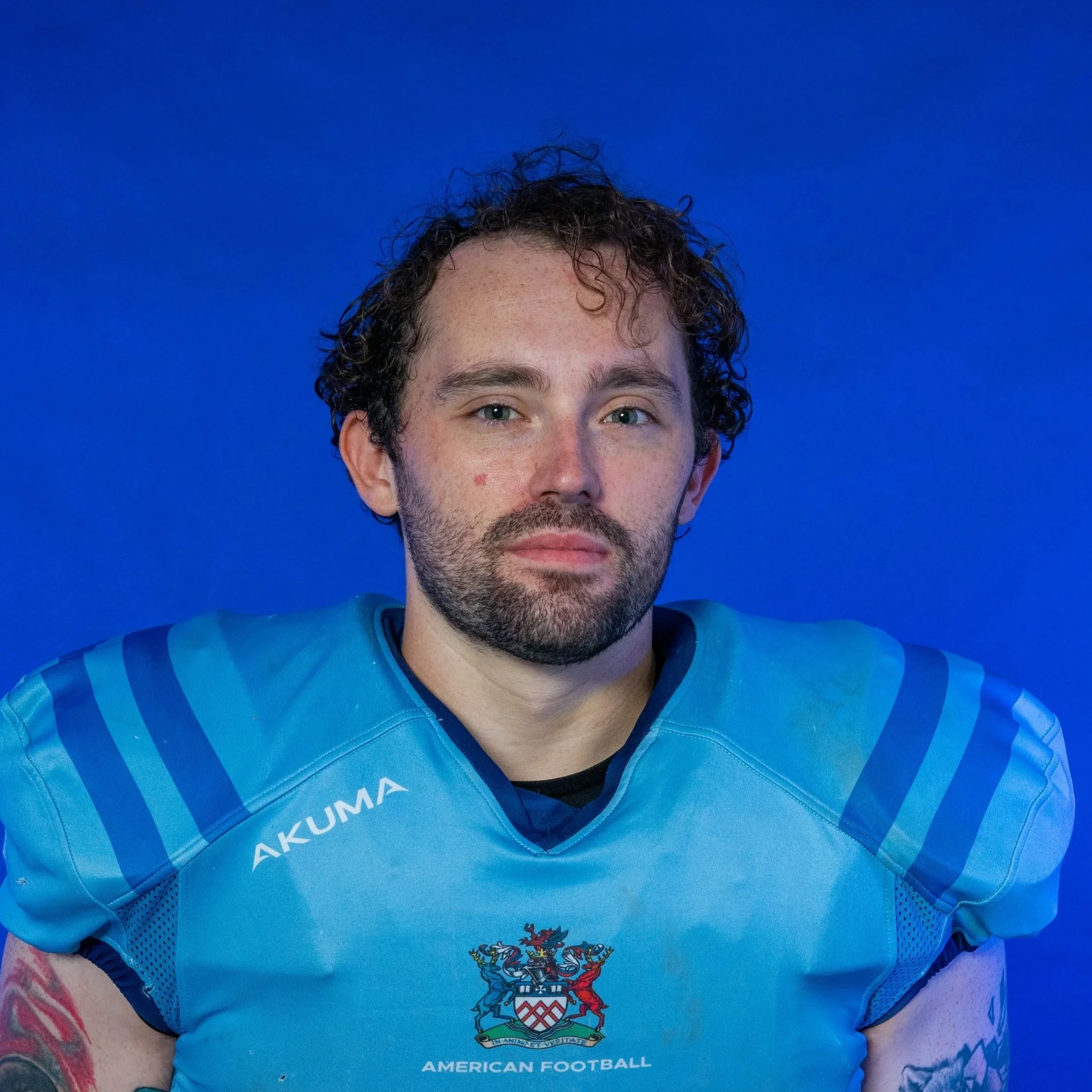 A football player wearing a blue helmet with 'Glads' written on it, a blue jersey with 'Team Glads' on the sleeve, and holding a football against a backdrop with the word 'Glads' and a Spartan helmet logo.