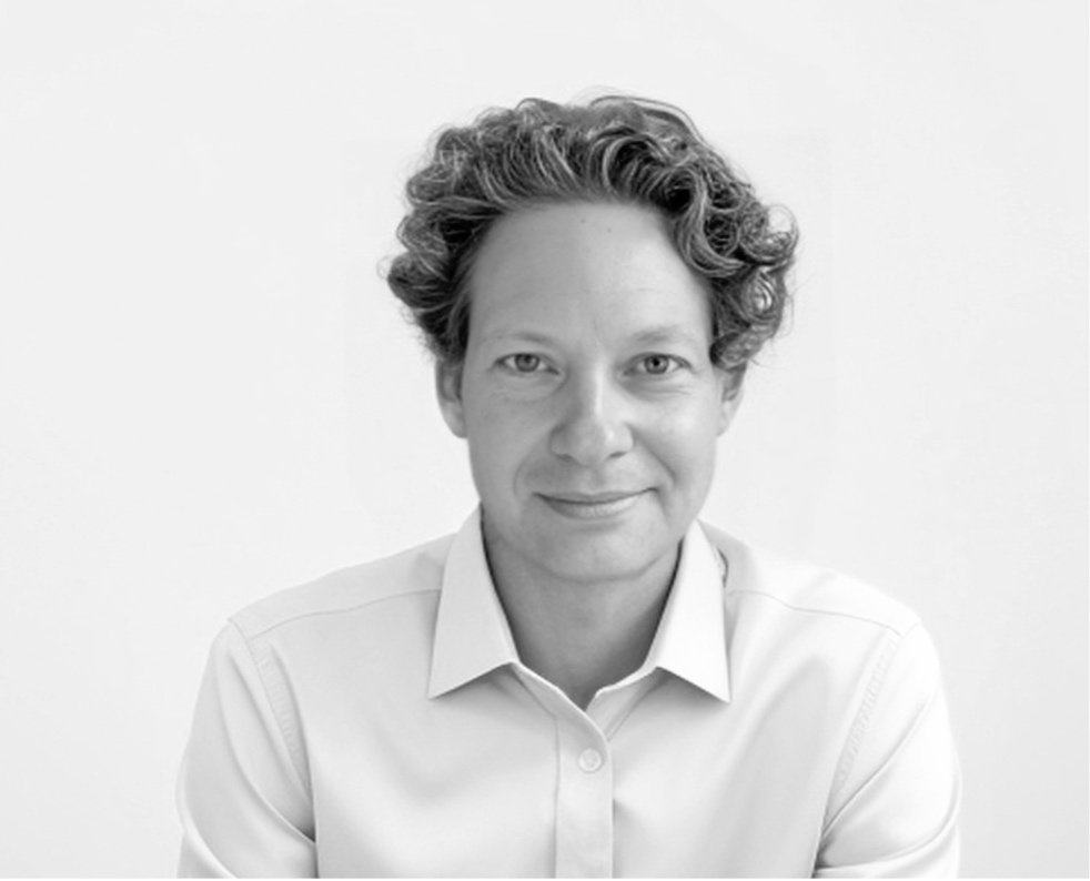 Black and white portrait of a woman with short, curly hair, wearing a collared shirt, looking at the camera with a slight smile, against a plain background.