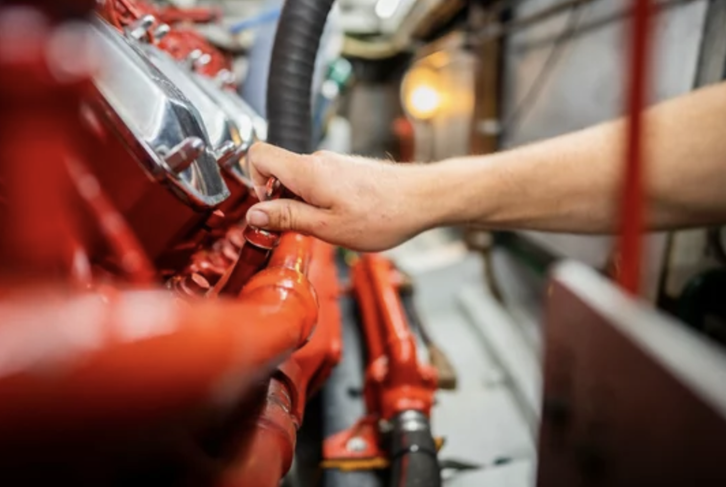 A person's hand adjusting or working on a red fire alarm control panel or some type of industrial control system.