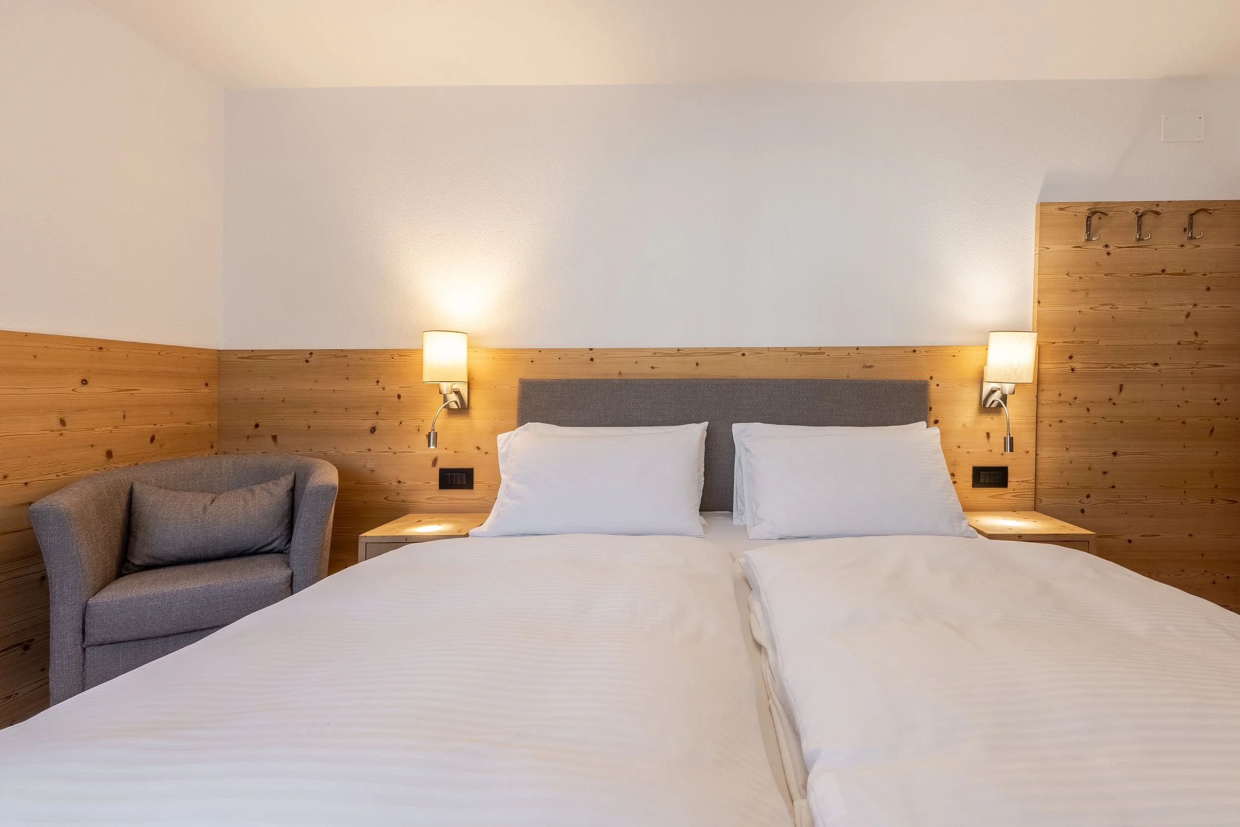 Camera da letto con letto matrimoniale, due cuscini bianchi, lampade da parete accese, pareti in legno e pareti bianche.