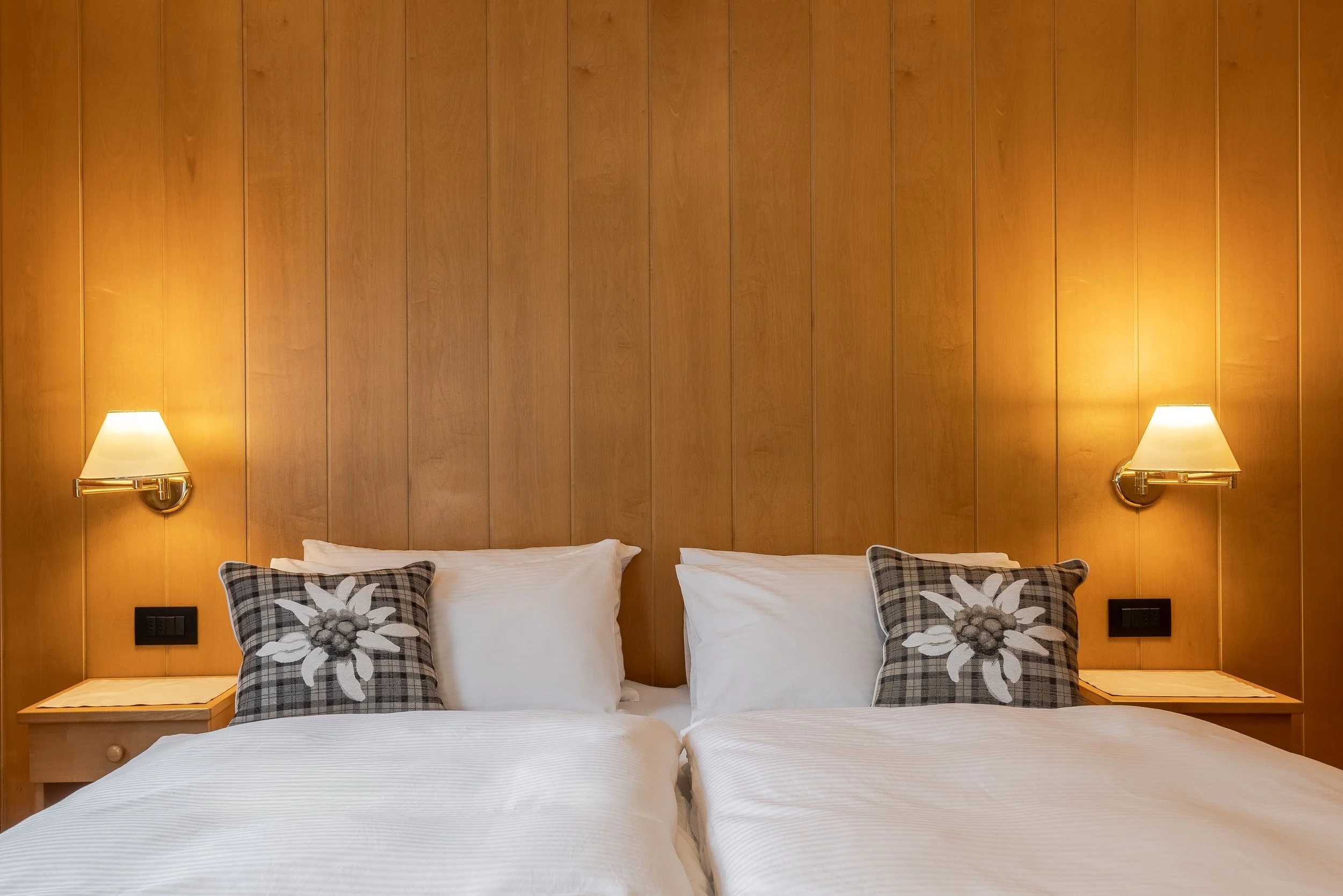 Letto matrimoniale con due cuscini decorativi a forma di fiore, testata in legno con luci da notte ai lati.