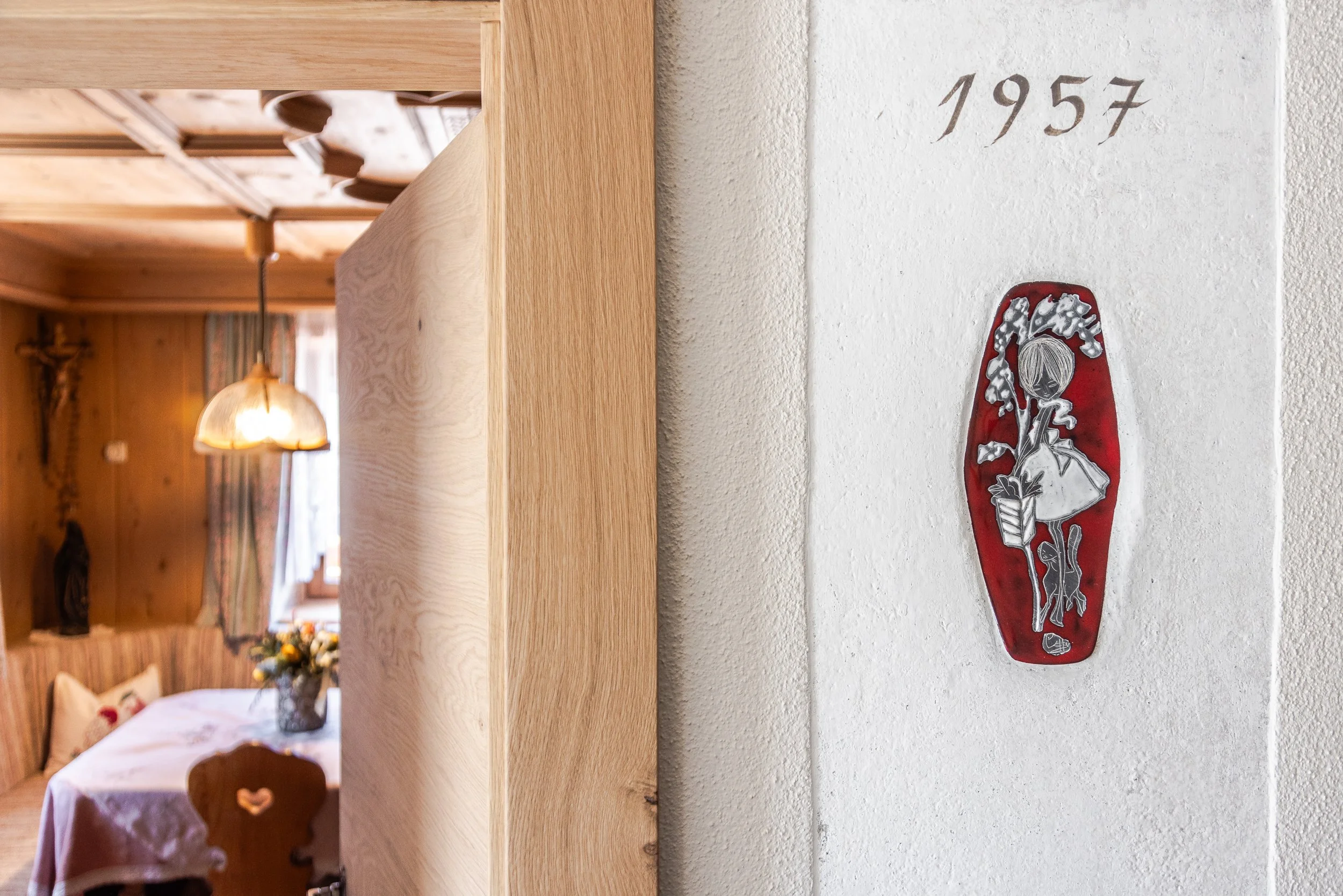 Una parete bianca con l'anno 1957 scritto e un'ornamentazione di una figura femminile stilizzata, con colori rosso, bianco e grigio.