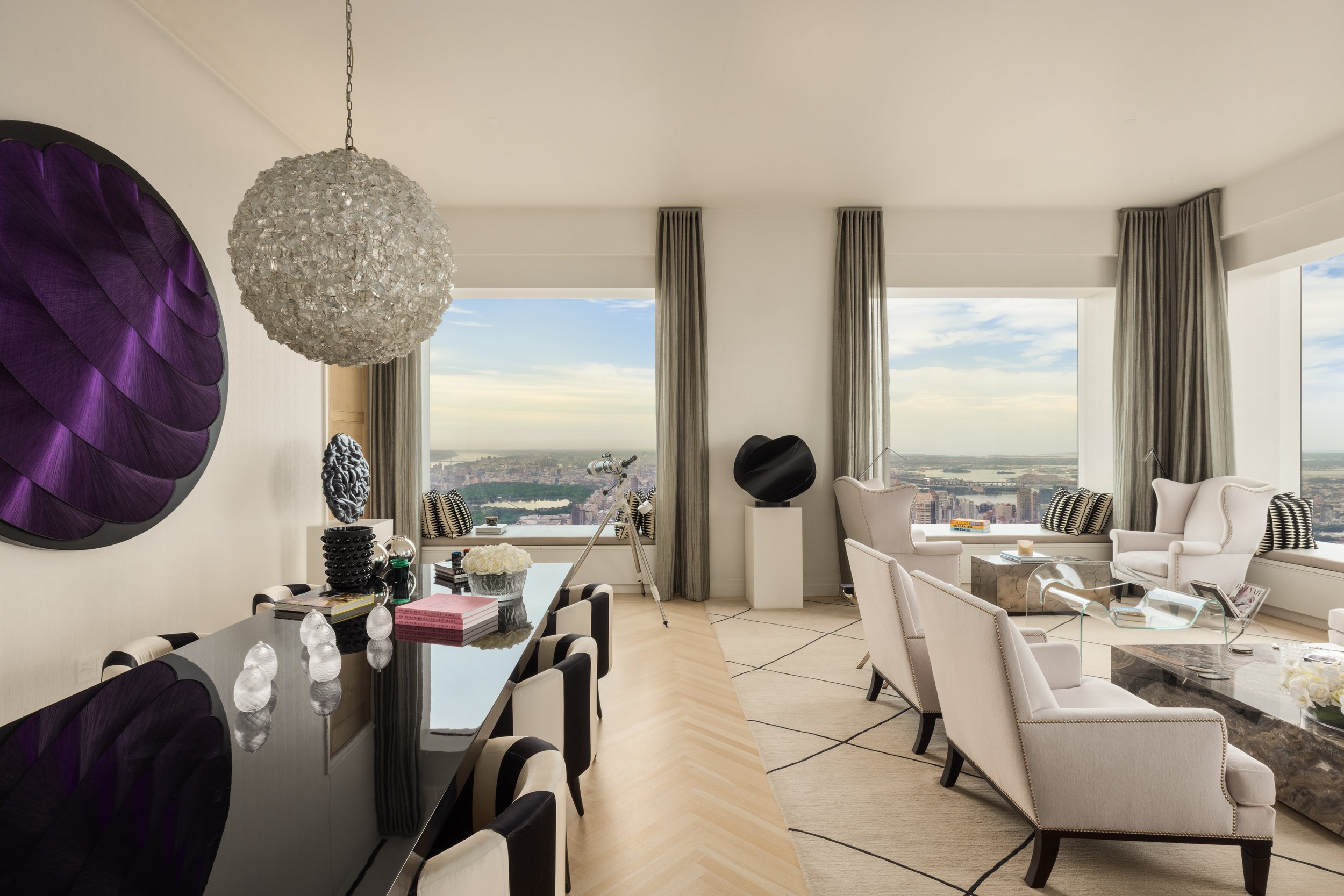 Modern living room with large windows, neutral-colored furniture, a glass coffee table, and decorative artwork on the wall.