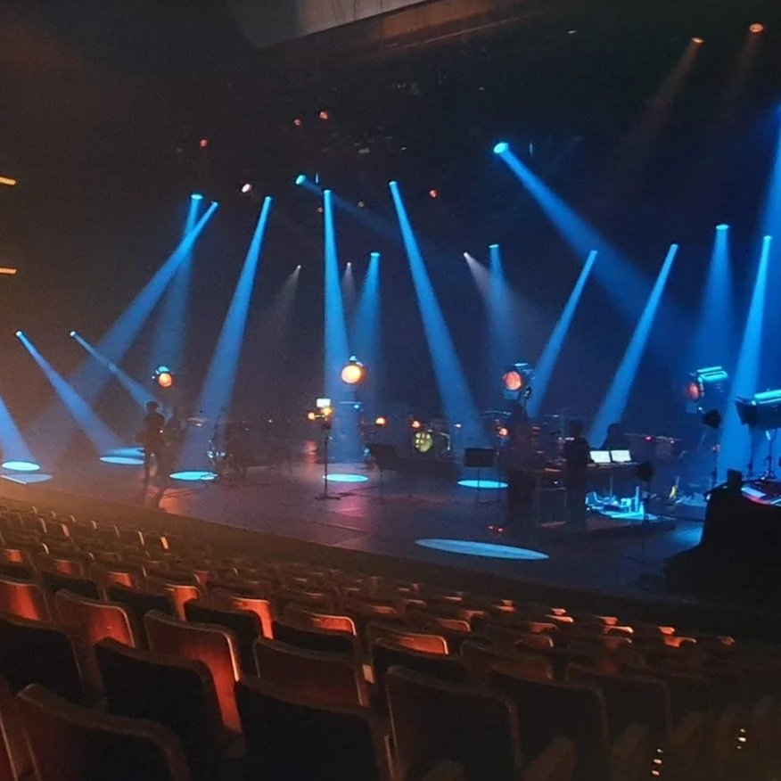 Empty theater stage with blue lighting and musical instruments set up, ready for a performance.