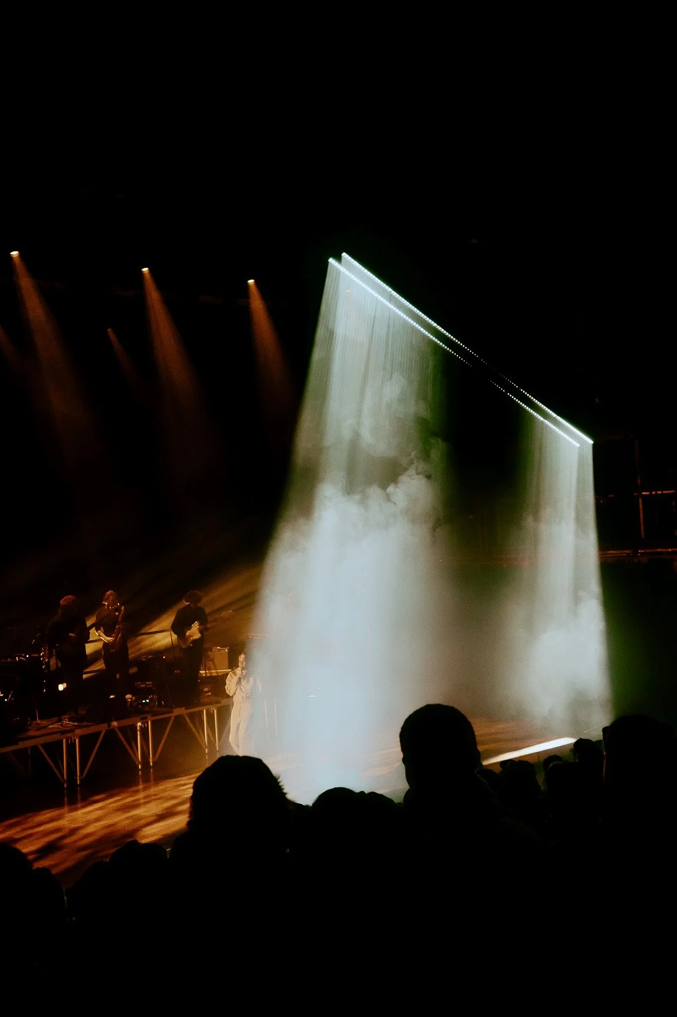 A stage with a band performing, with colorful stage lighting, smoke effects, and silhouetted audience members.