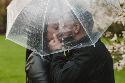 Engaged+couple+kiss+under+umbrella+at+raining+engagement+photoshoot+photo+by+Fedora+Media.webp