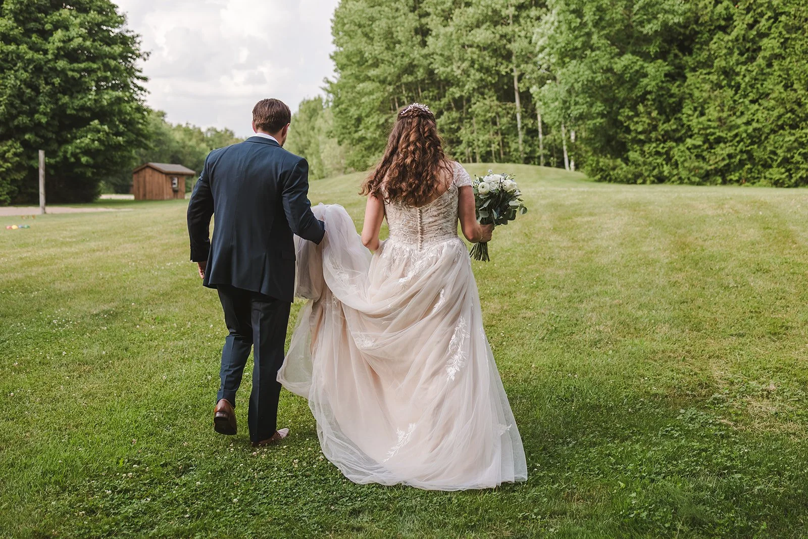 Groom walking with bride while carrying train  CJ Country events  Guelph, ON  Fedora Media.jpg