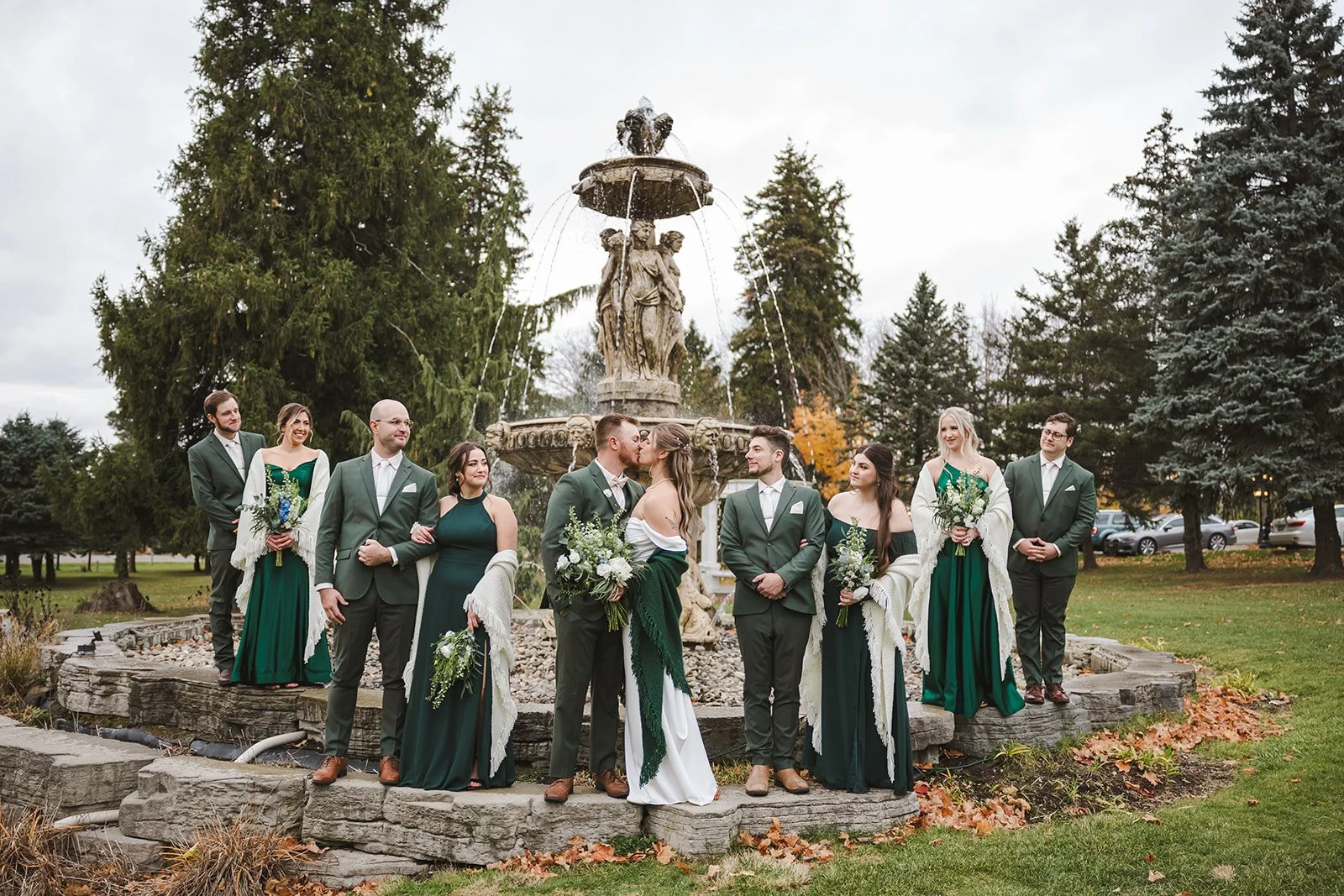 Bride and groom kiss in fron of fountain with wedding party  fall wedding  Fedora Media.jpg