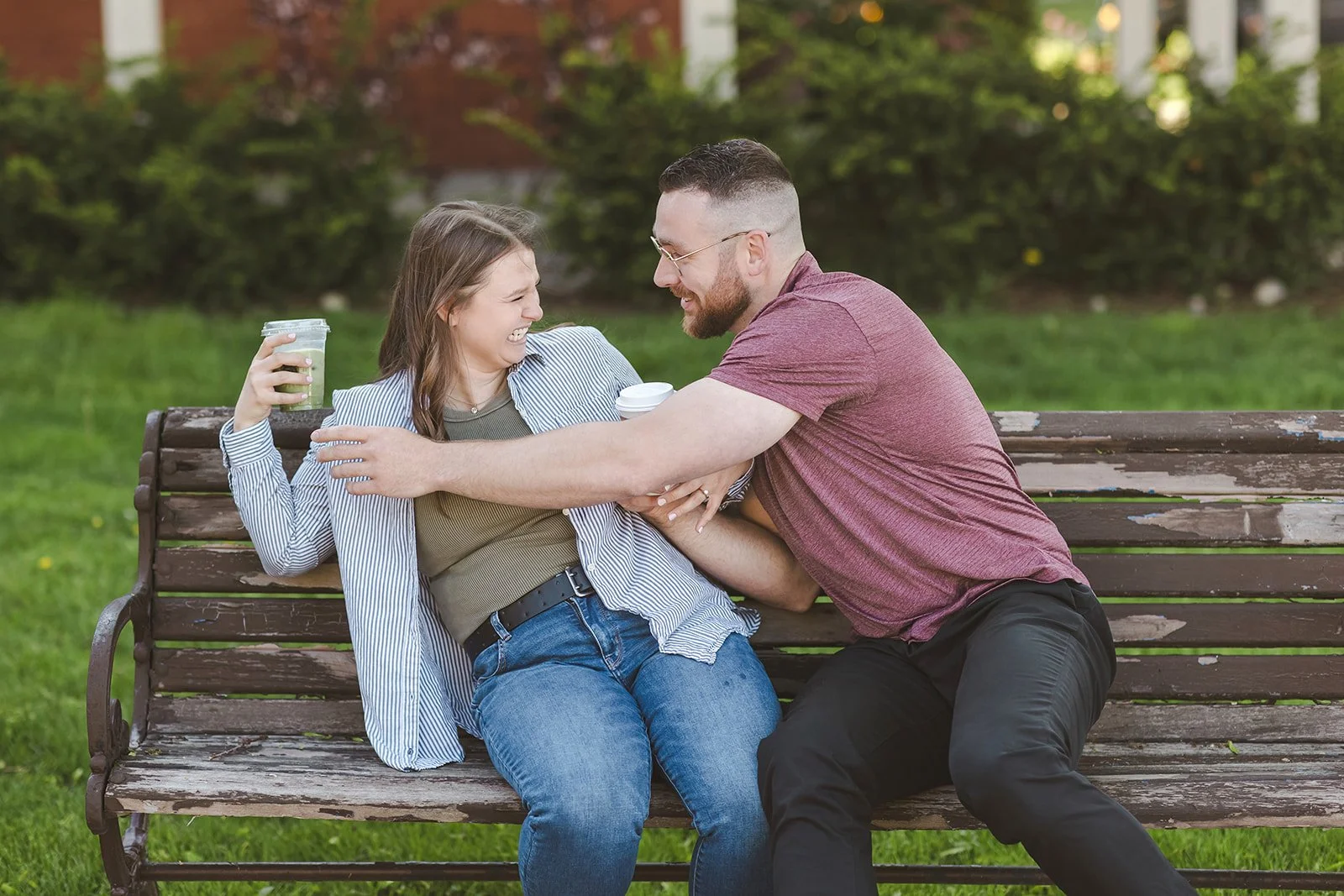 Couple sitting on park bench playfully fighting over coffee  Ontario Engagement  Fedora Media.jpg