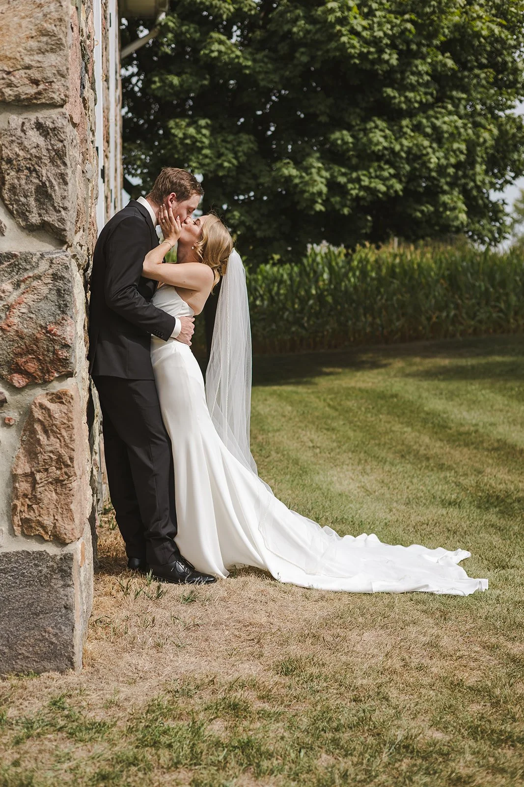 Bride grabs grooms face for a kiss against stone wall Straford, ON  Fedora Media.jpg