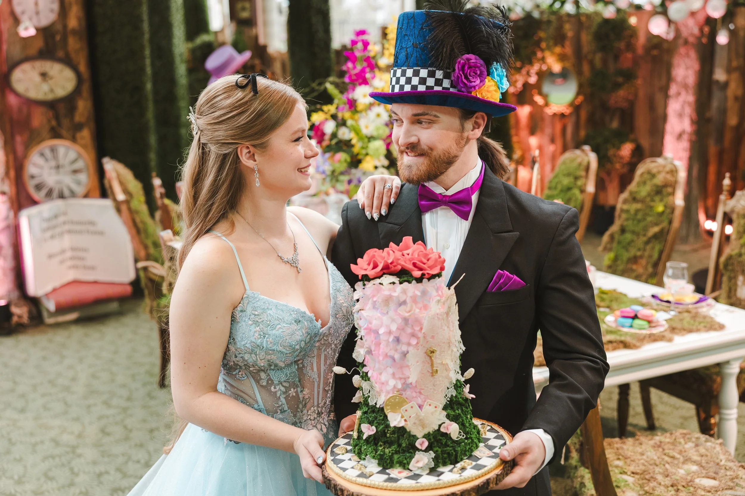 bride-and-groom-posed-with-floral-cake-alice-in-bloomland-fedora-media.jpg