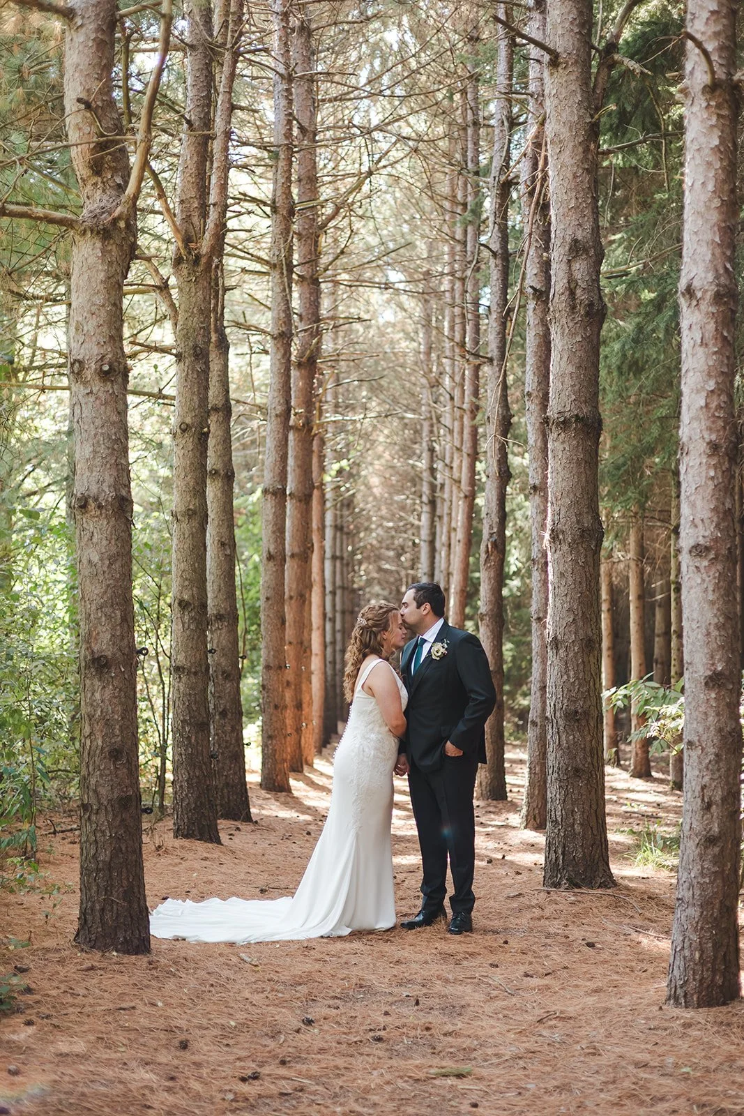 Groom kissing bride's forehead in forest  Erin Estates  Fedora Media.jpg
