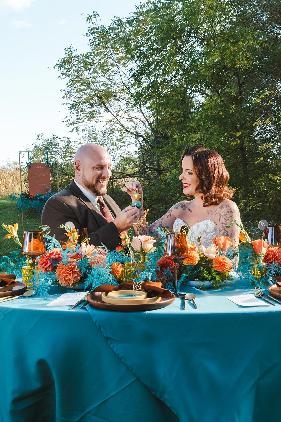 Bride and Groom holding chocolate strawberries seated at colourful table setting  Great Lakes Helicopters  Fedora Media.jpg