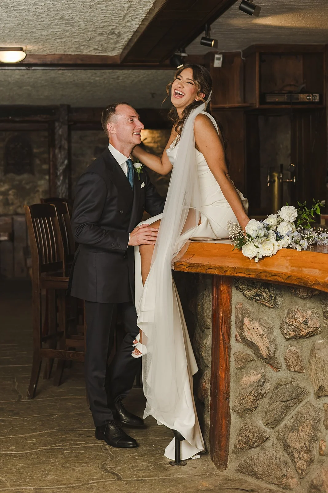 Bride sitting on bar with groom standing beside her  River's Edge  Arlington Hotel  Paris, ON  Fedora Media.jpg