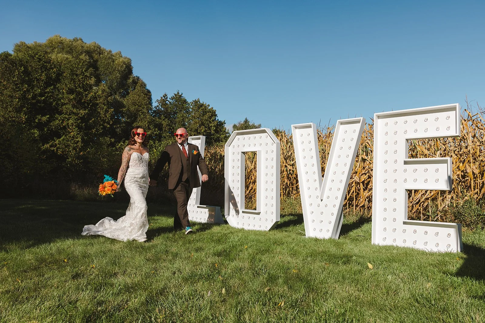 Bride and Groom holding hands walking with bouquet in front of love sign  Great Lakes Helicopters  Fedora Media.jpg