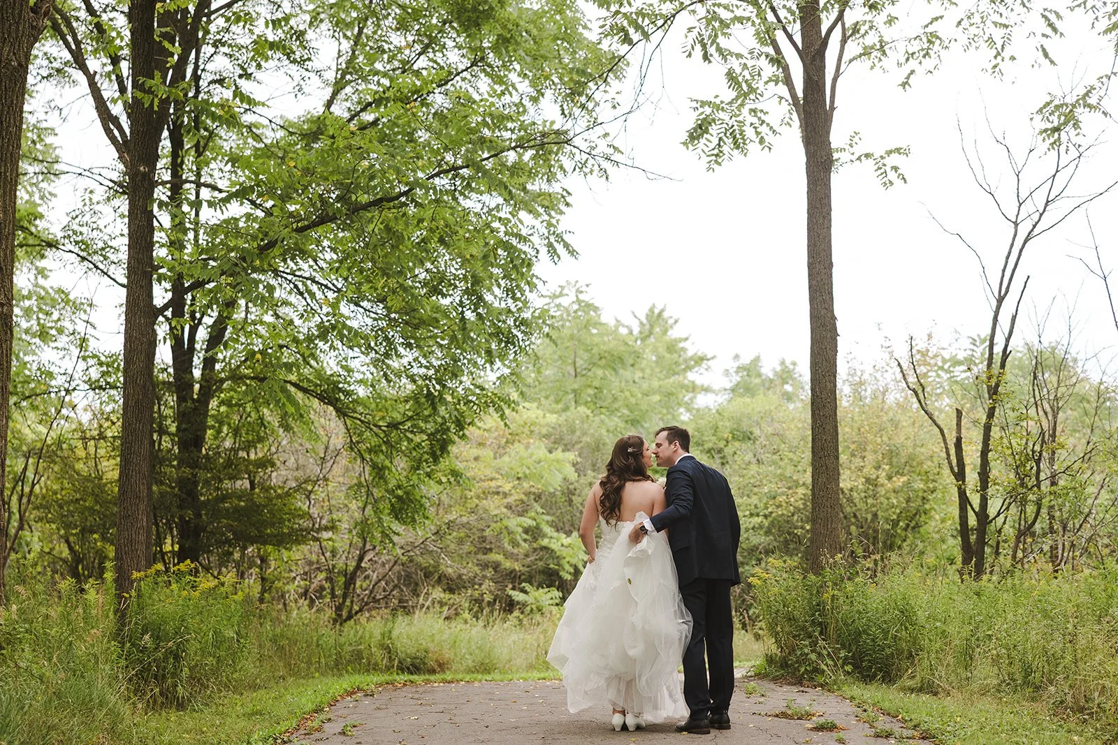 Bride and groom walking through forest stop for a kiss  Carmen's Hotel  Hamilton, ON  Fedora Media.jpg